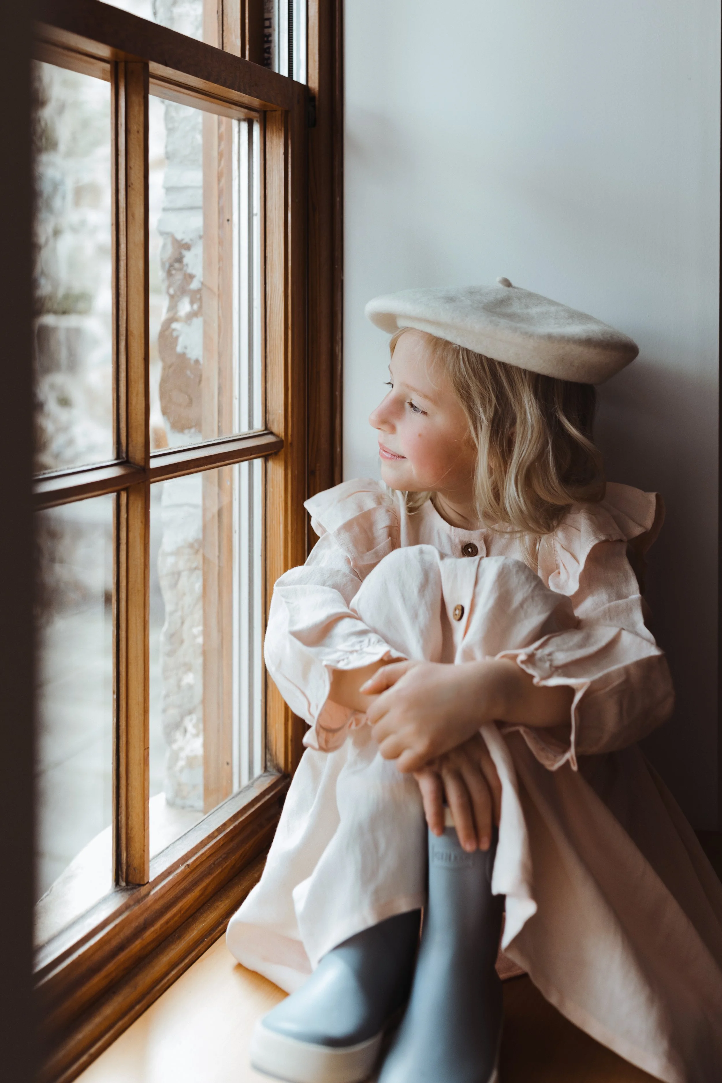 Young girl sits in window seat wearing linen and white beret.