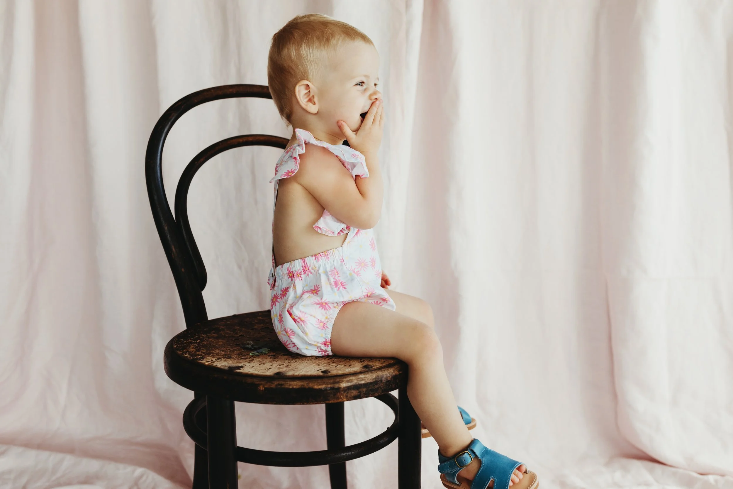 Baby smiles as she sits on chair in kids label photo shoot in Tasmania.