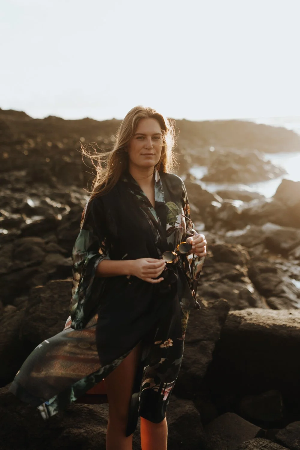 Woman stands at rocky beach in fashionable kimono.