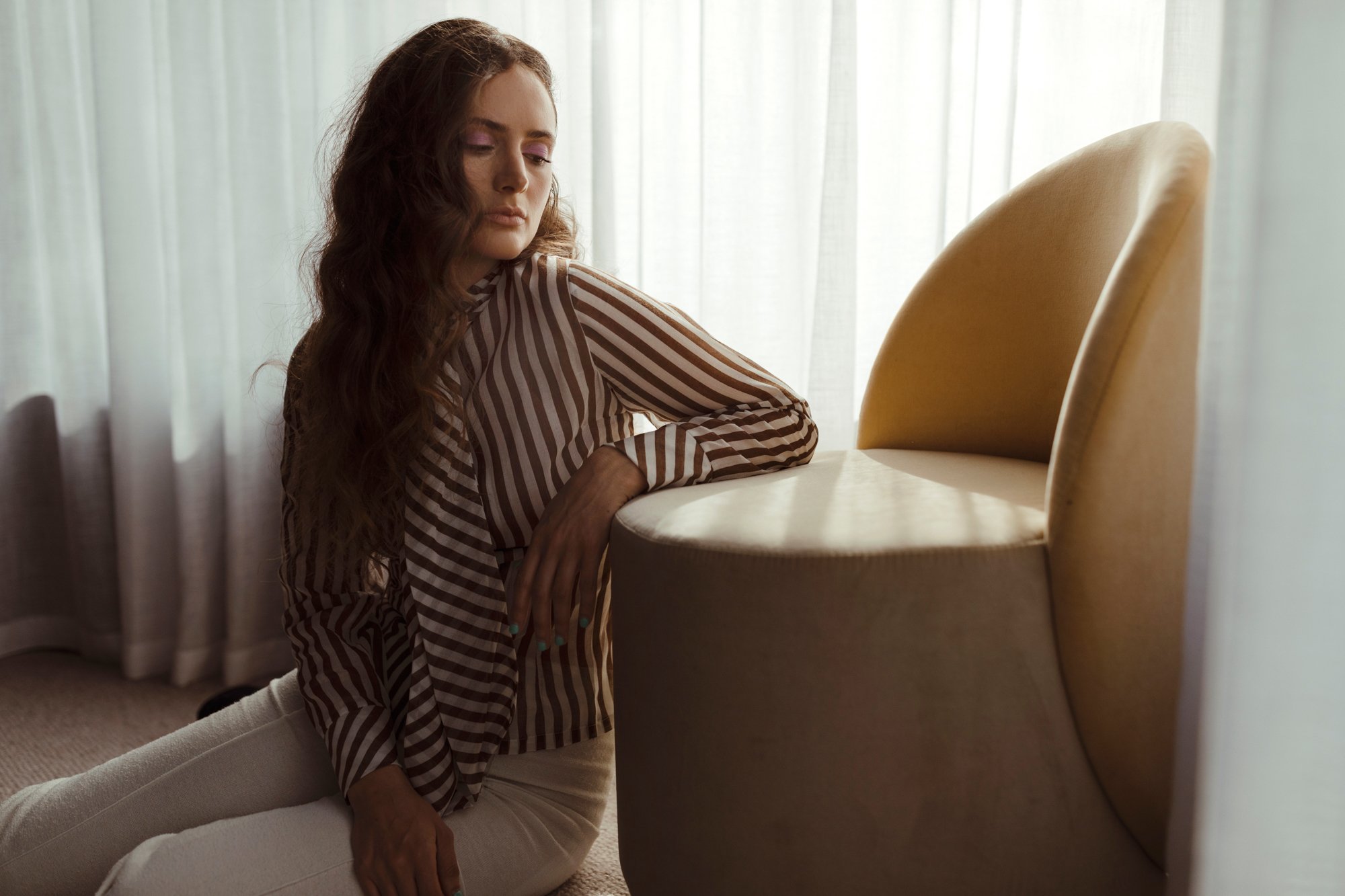 Model poses against designer chair for styled photo shoot.