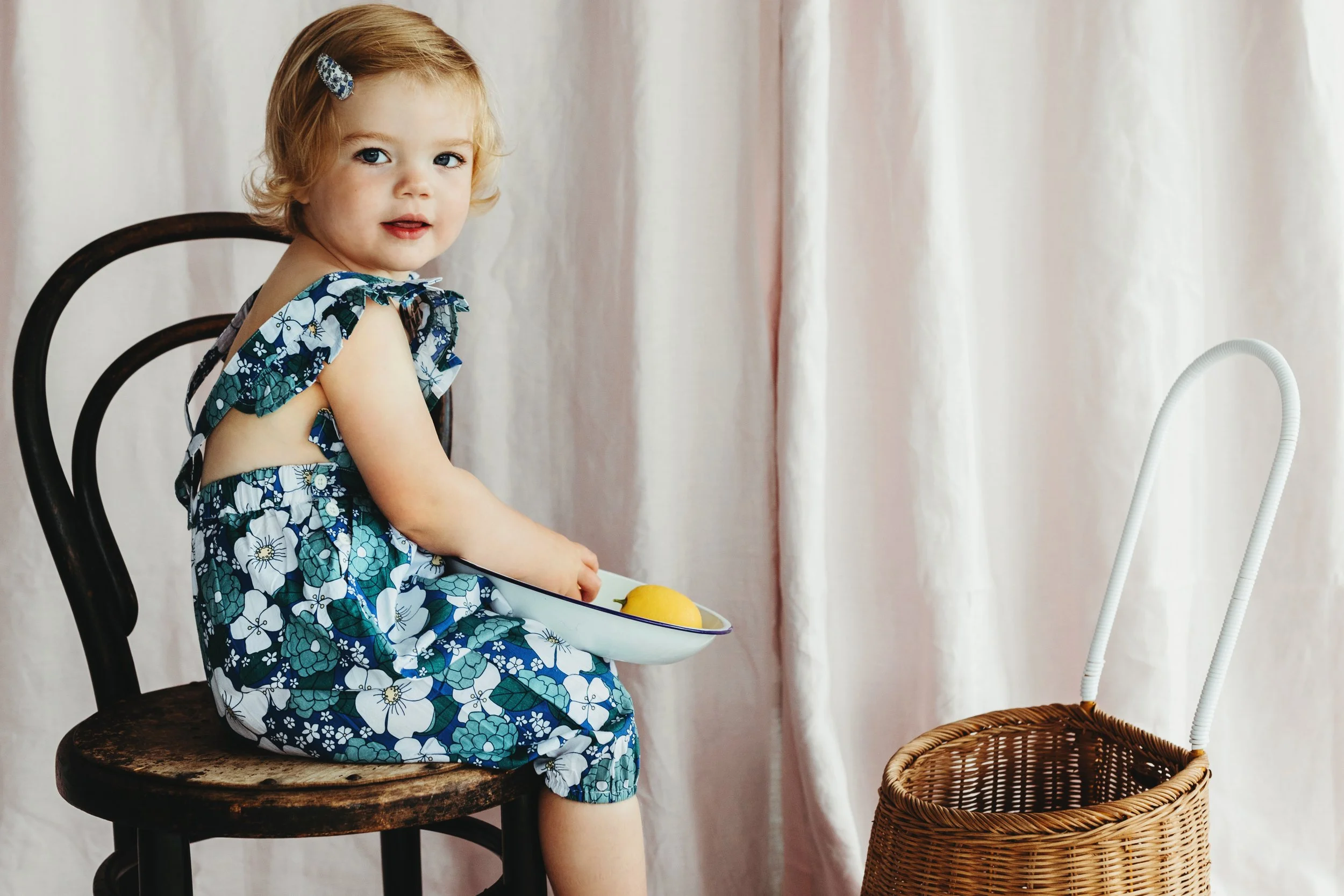 Toddle sits on bentwood chair holding bowl of lemons in studio shoot.