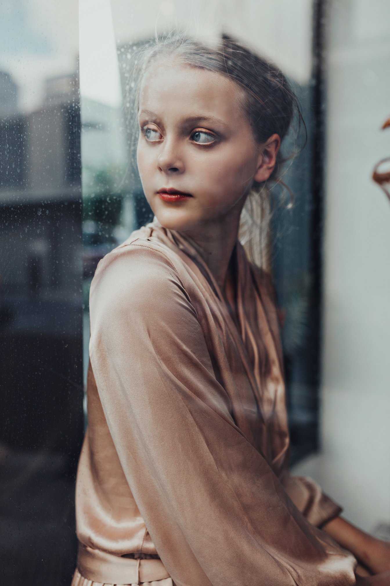 Young woman looks through window wearing classic fashionable dress.