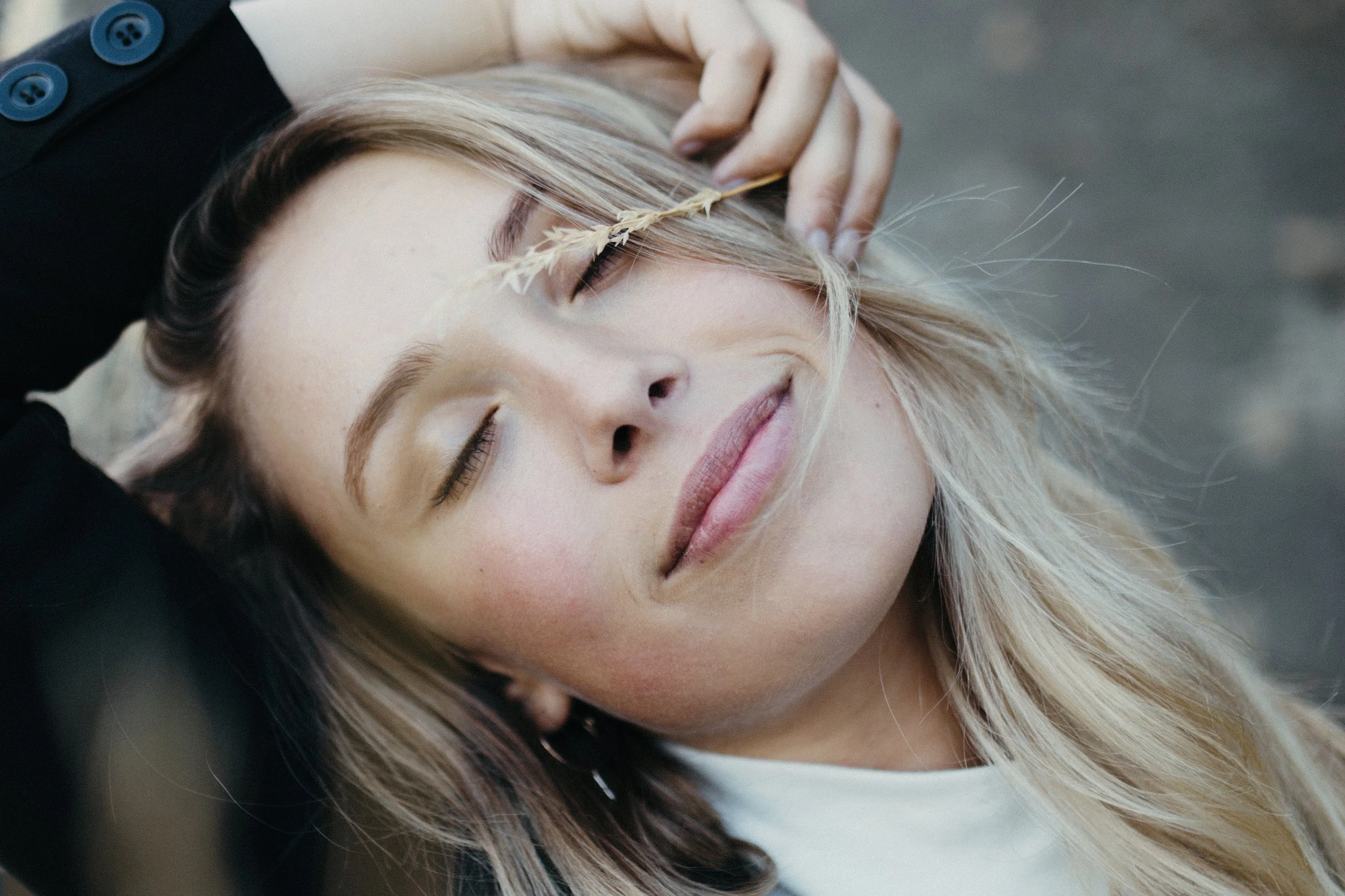 Woman has a peaceful look as she closes her eyes and holds dry grass against her face.
