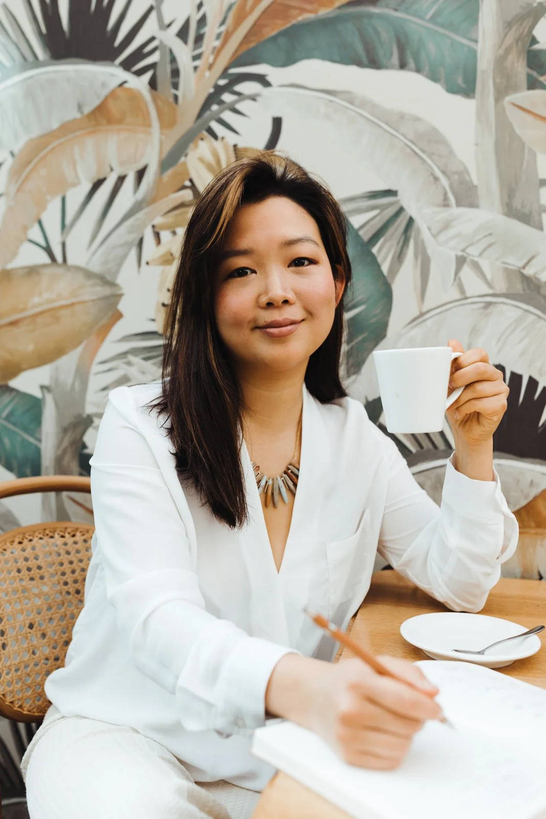 Woman holds cup of tea and takes notes for personal branding photo session.