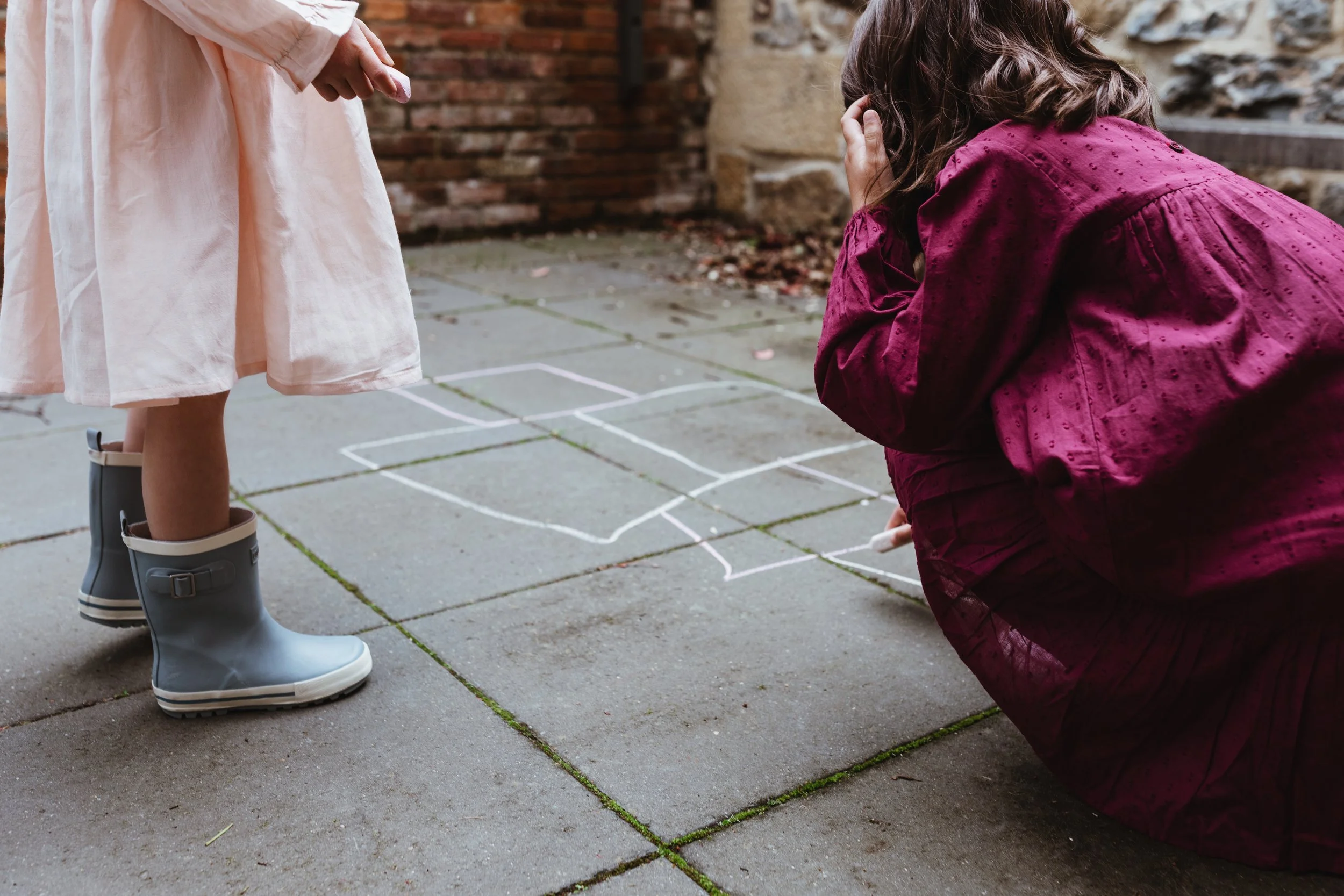 Two girls play hopscotch in courtyard for styled fashion photo shoot.