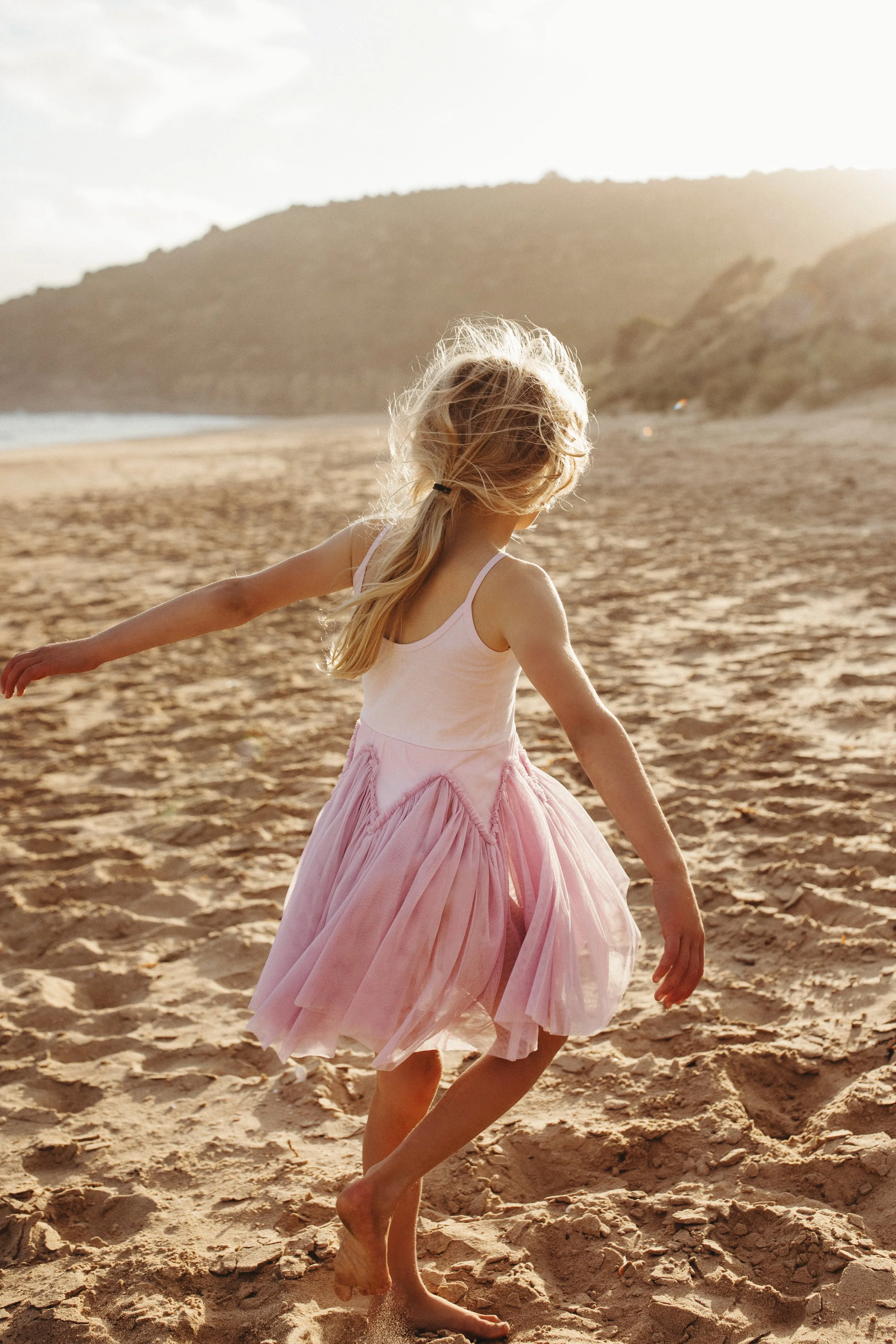 Young girl walks on beach at sunset in pink dress.