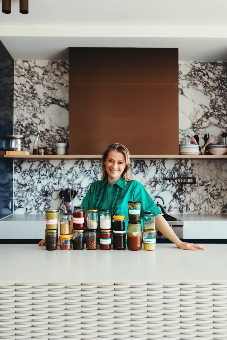 Katrina Meynink poses behind jars of condiments in beautiful kitchen.