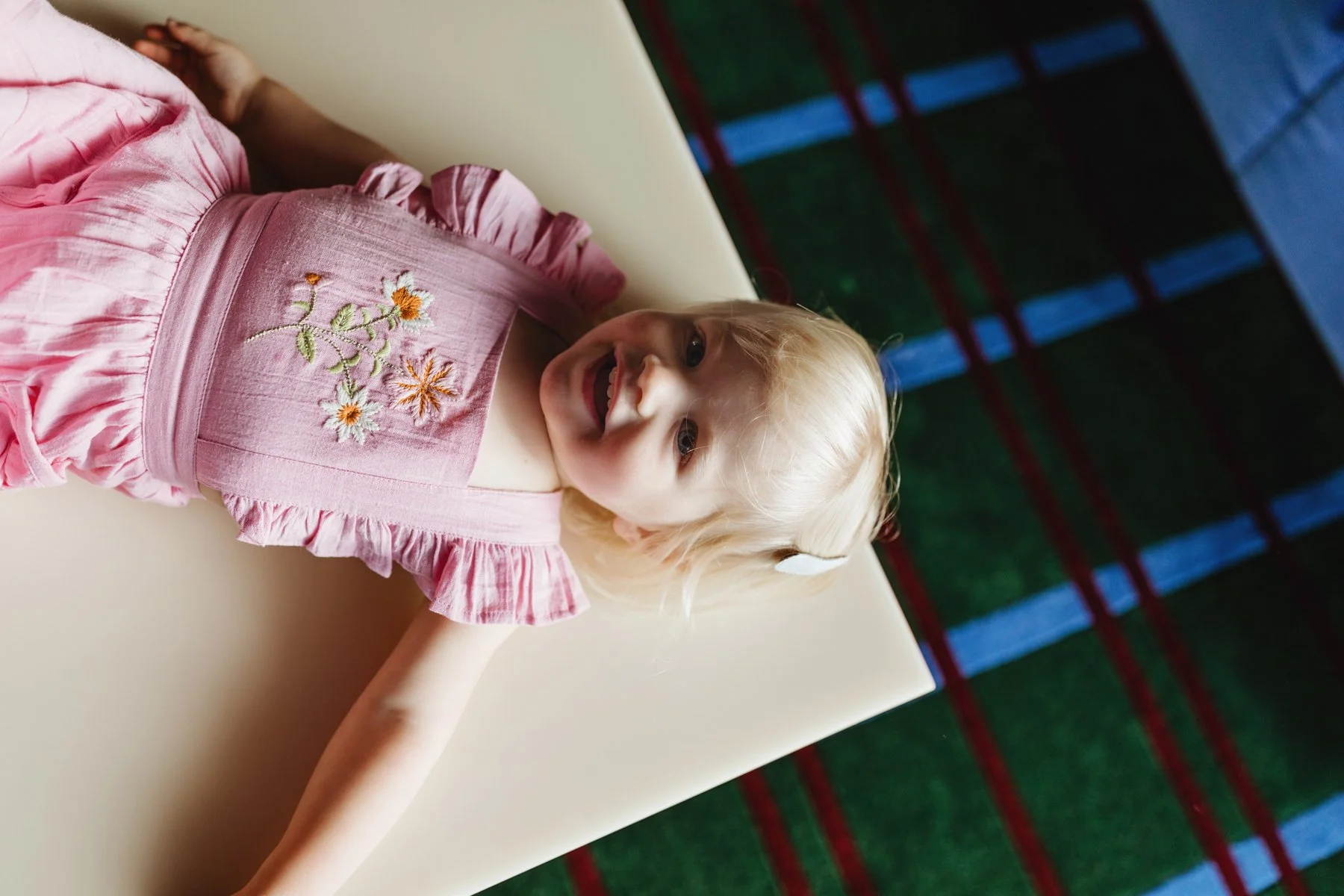 Toddle lays down in pink dress for fashion photo shoot.