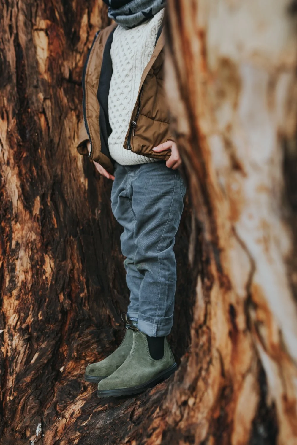 Child stands in tree branches wearing Blundstone boots in Tasmania.