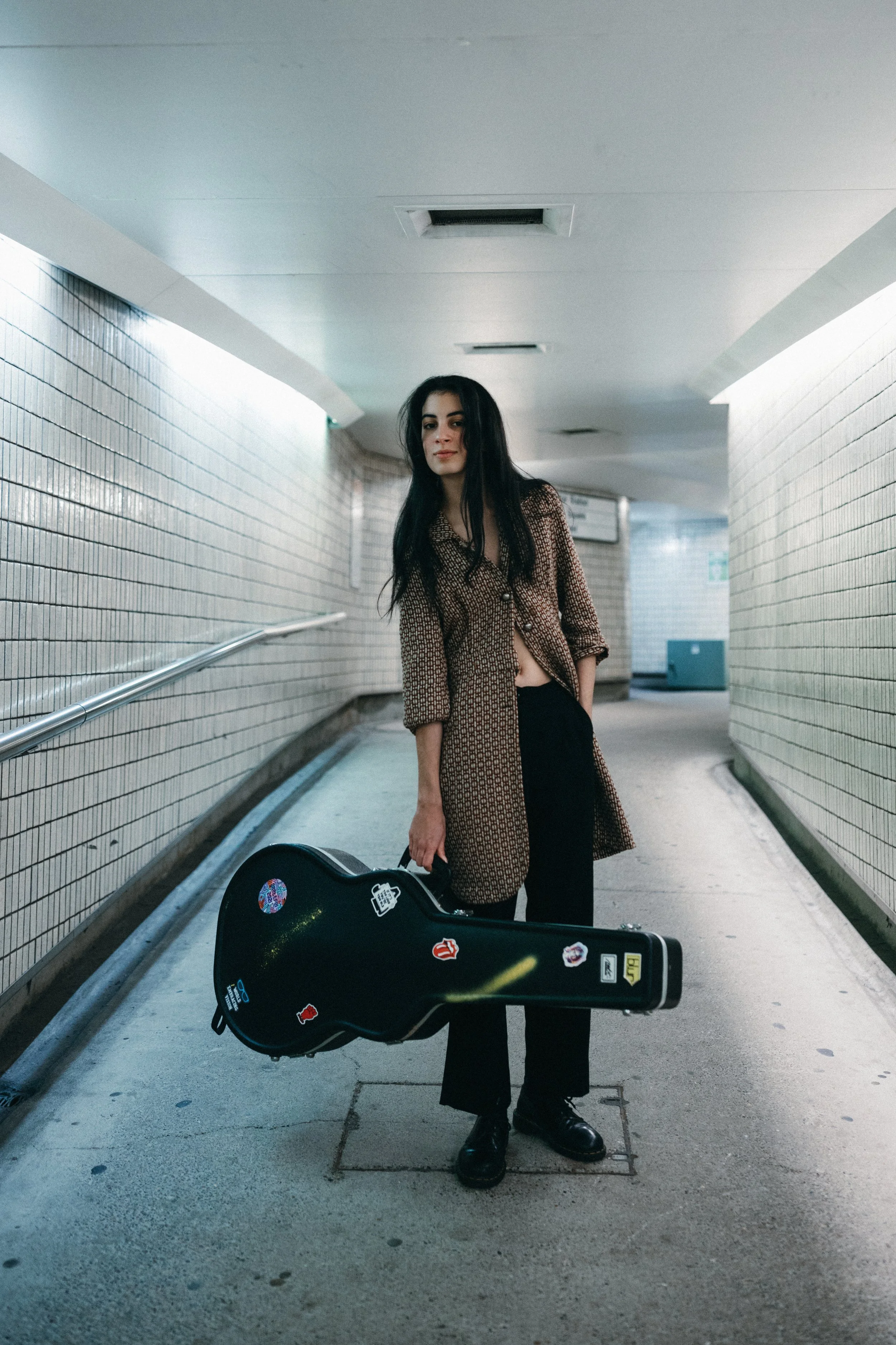 Musician stands in subway with guitar for branding photo shoot.