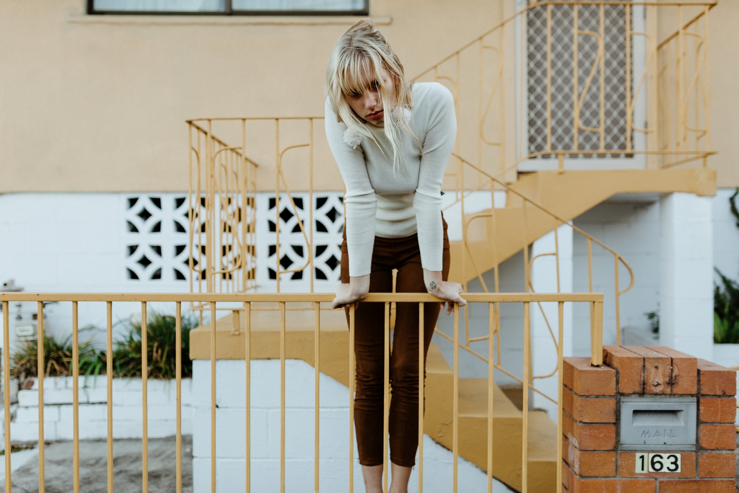 Model leans over railing in retro fashion photo shoot.