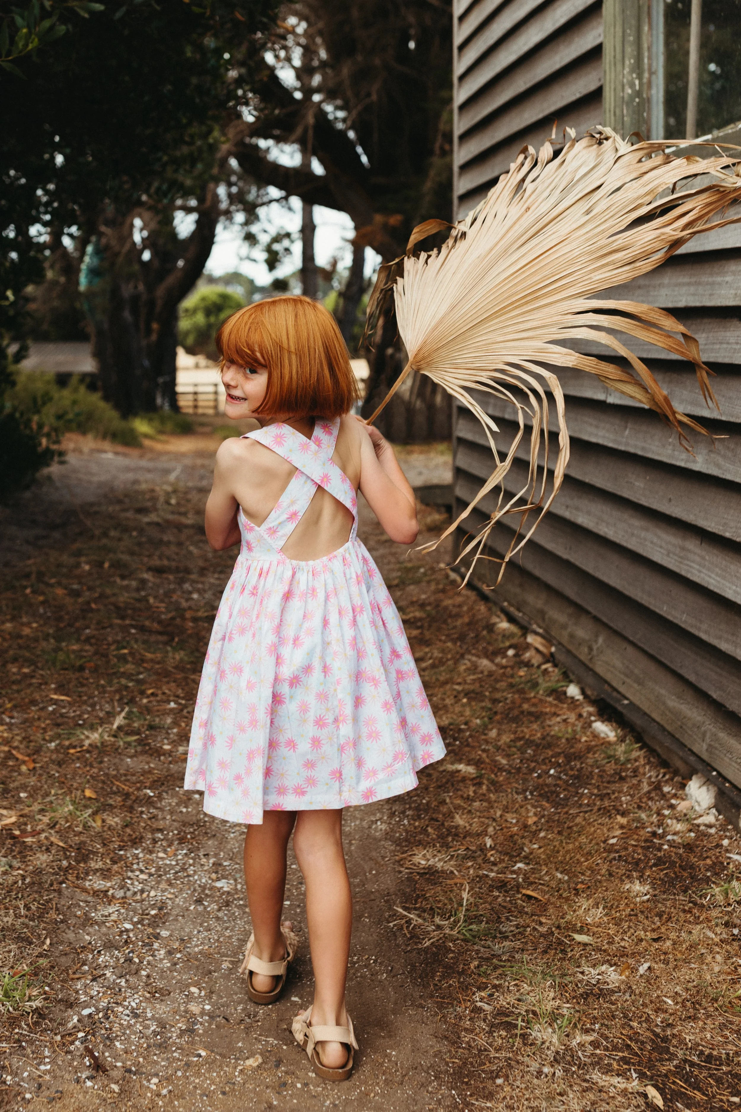 Young girl walks with palm frond in pink dress.
