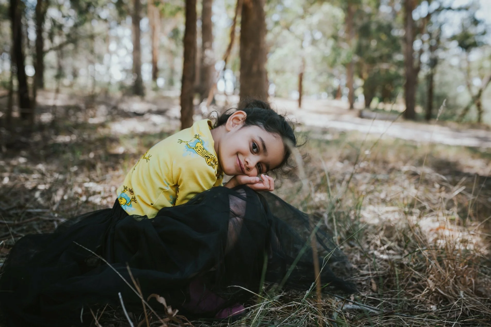 Young girl sits and smiles in parkland for kids clothing label photo shoot.