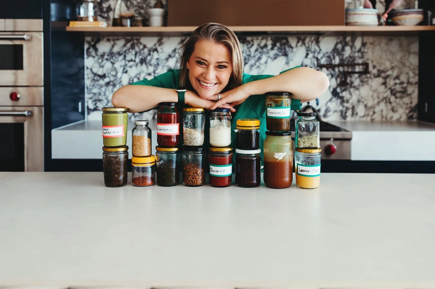 Katrina Meynink smiles with jars of condiments for recipe book commercial photos.