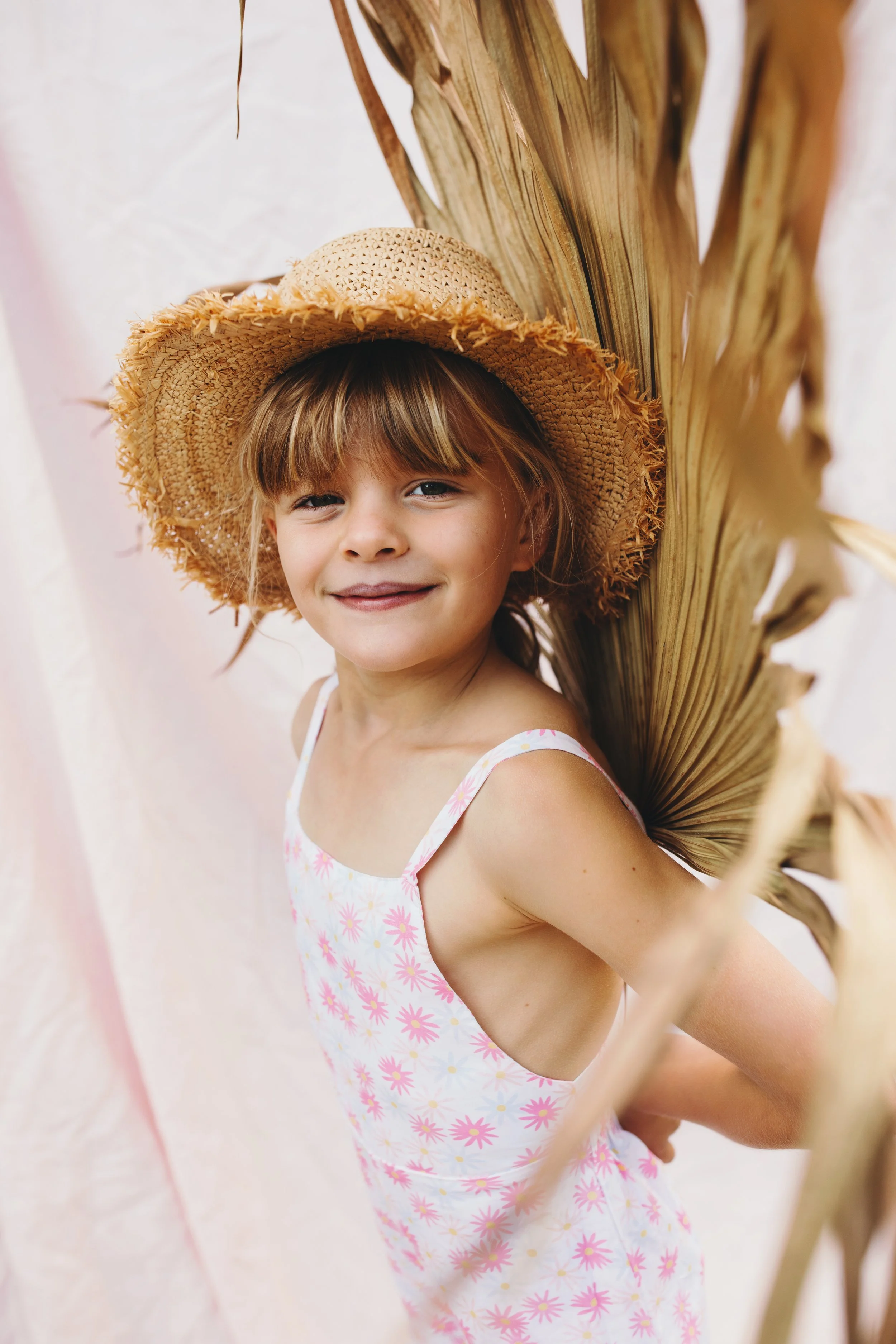 Girl stands with palm frond and smiles in photography studio.