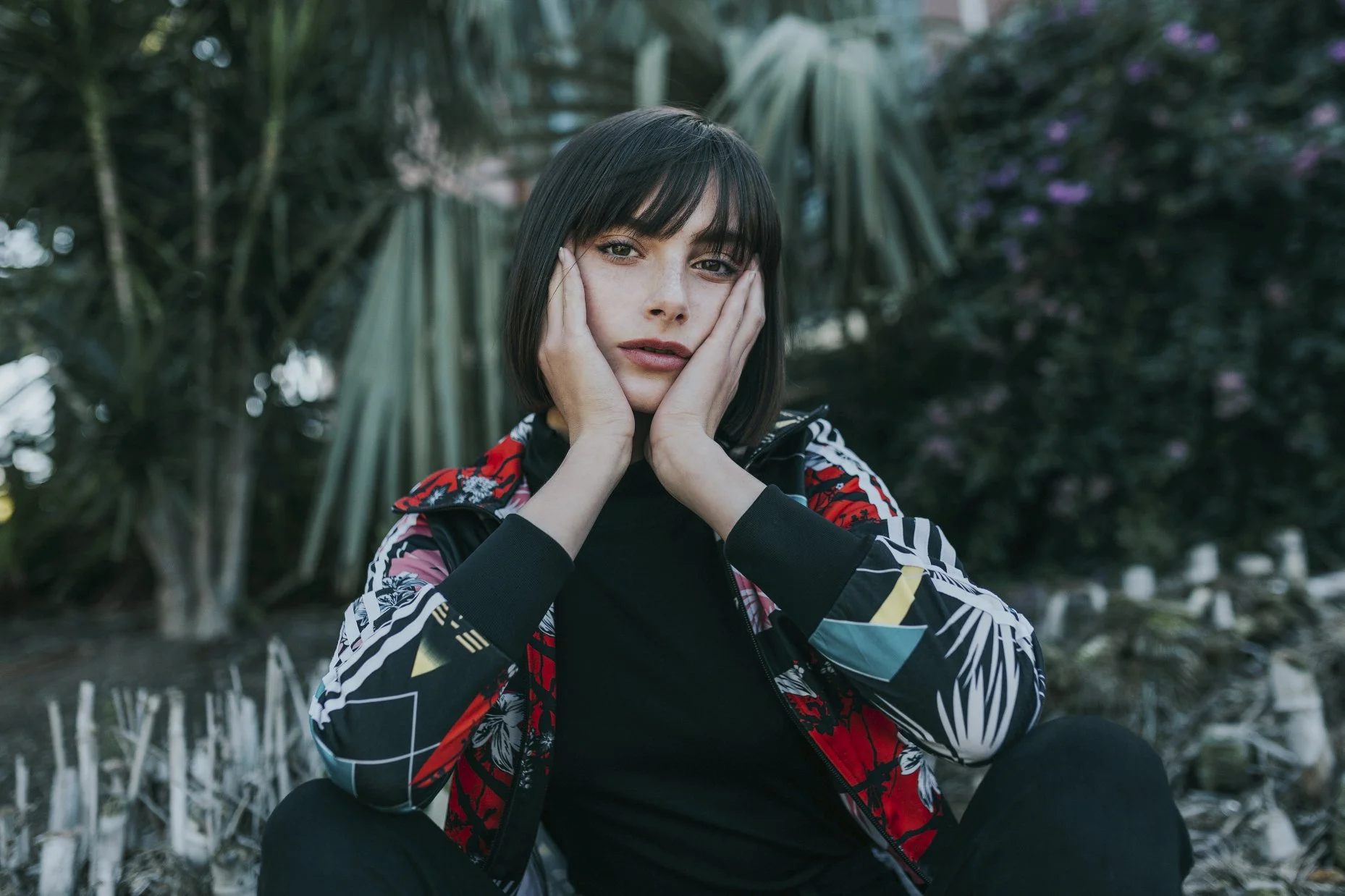 Model rests face in her hands as she sits in garden.