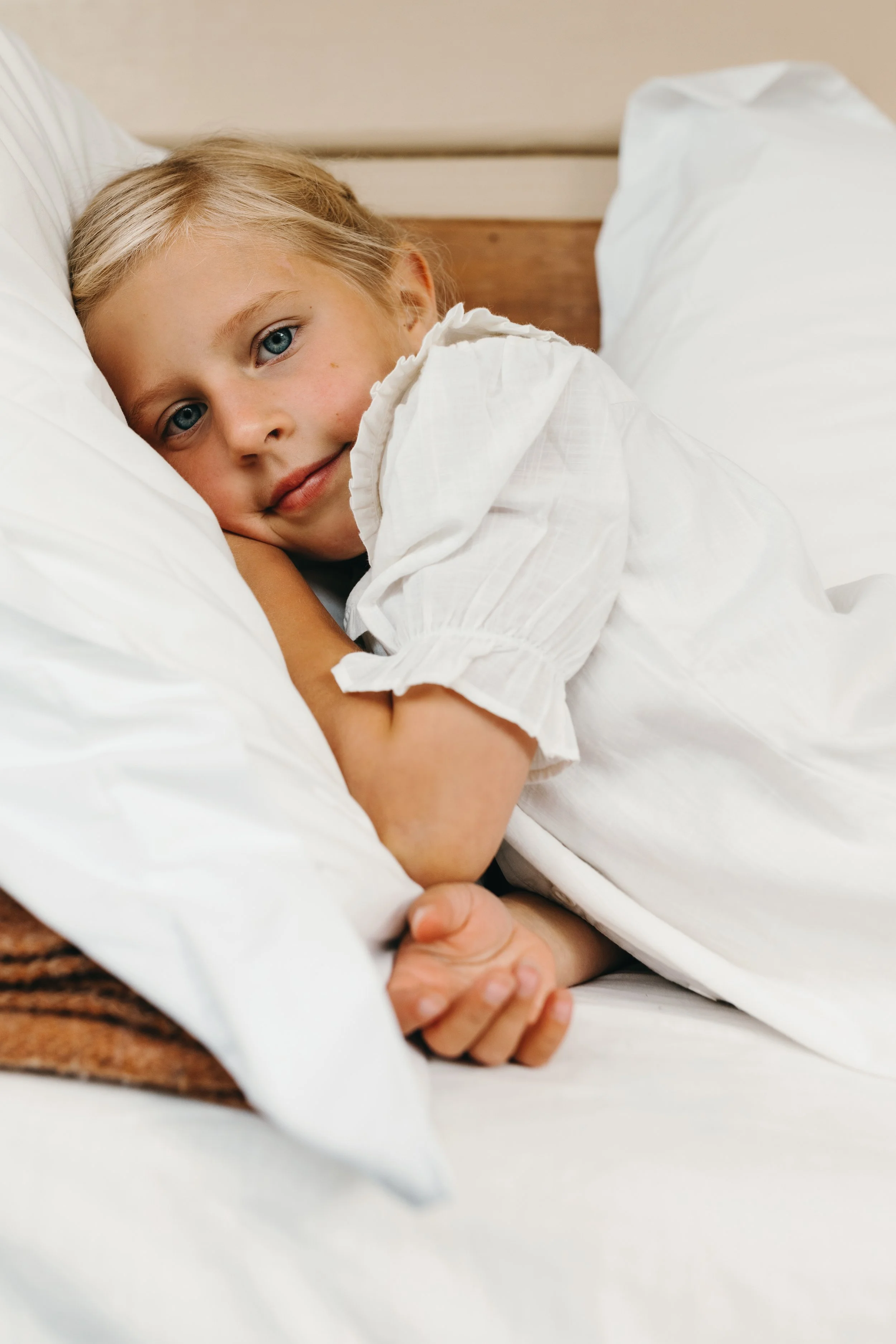 Young girl lays in bed wearing white pyjamas.