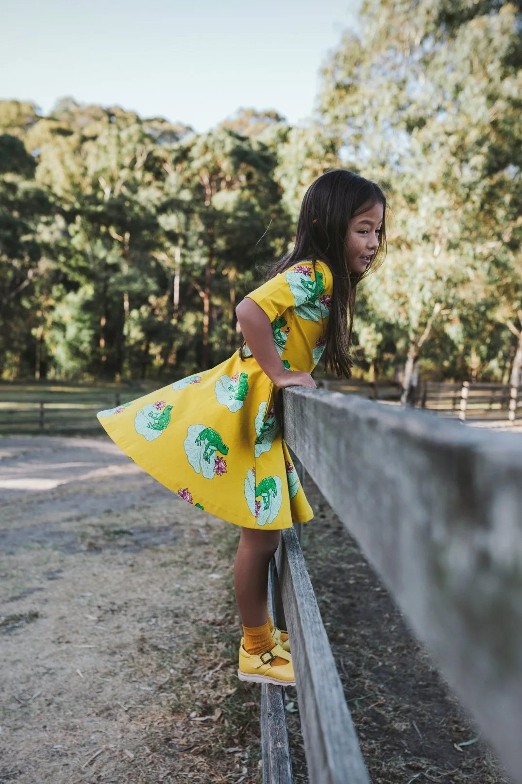 Girl climbs fence in bright yellow dress during photo shoot in Melbourne.