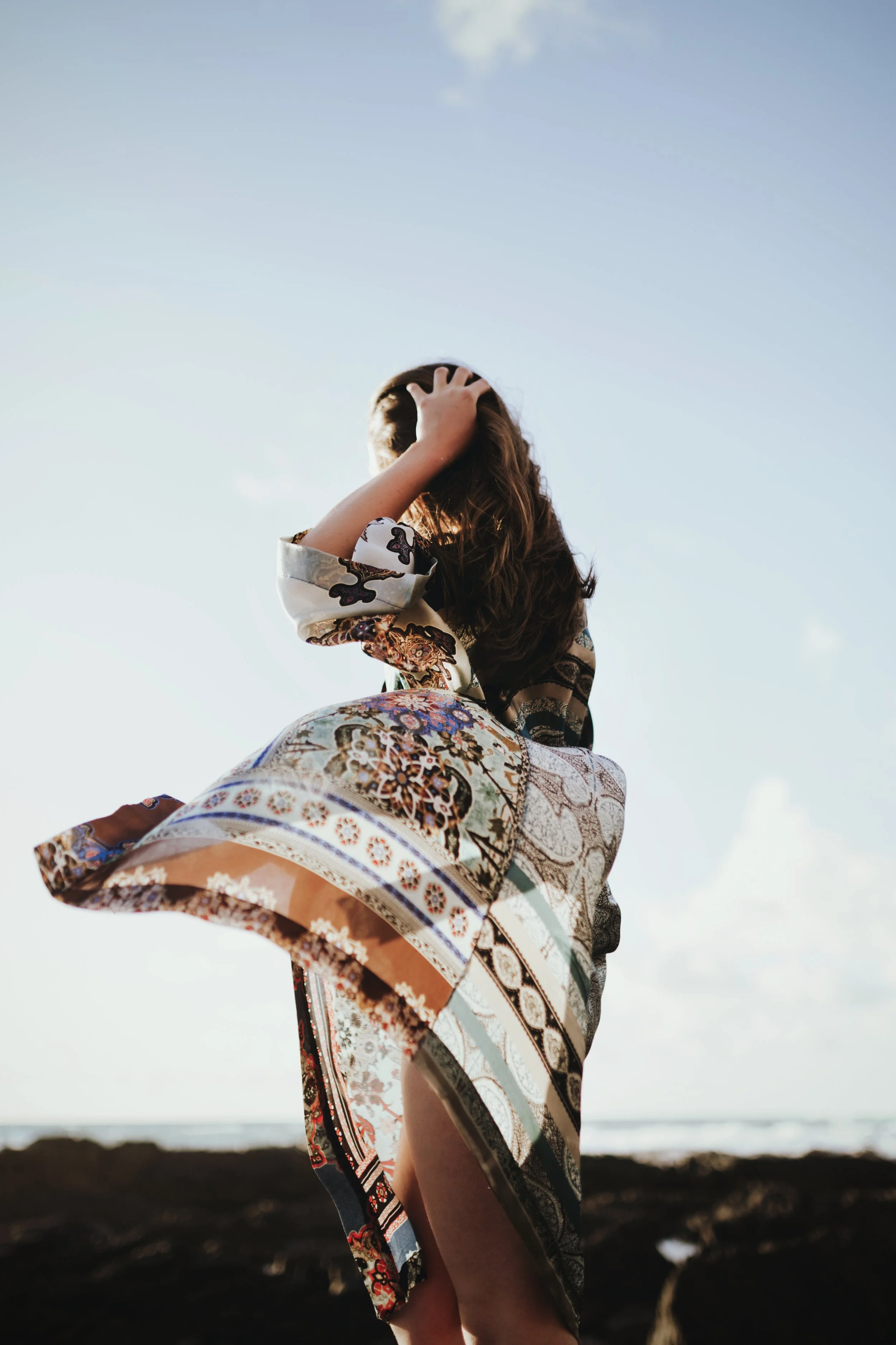 Woman stands as wind takes her silk kimono at the beach.