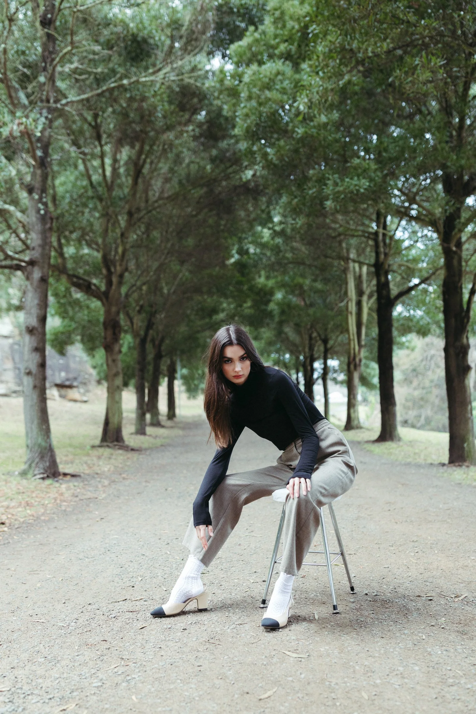 Woman poses in park with black top and vintage pants.