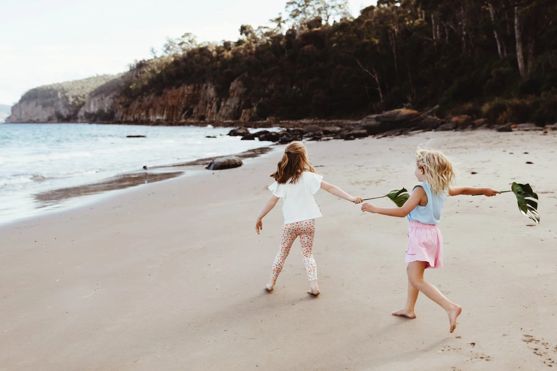Children run on beach in cute clothing for commercial photo shoot.