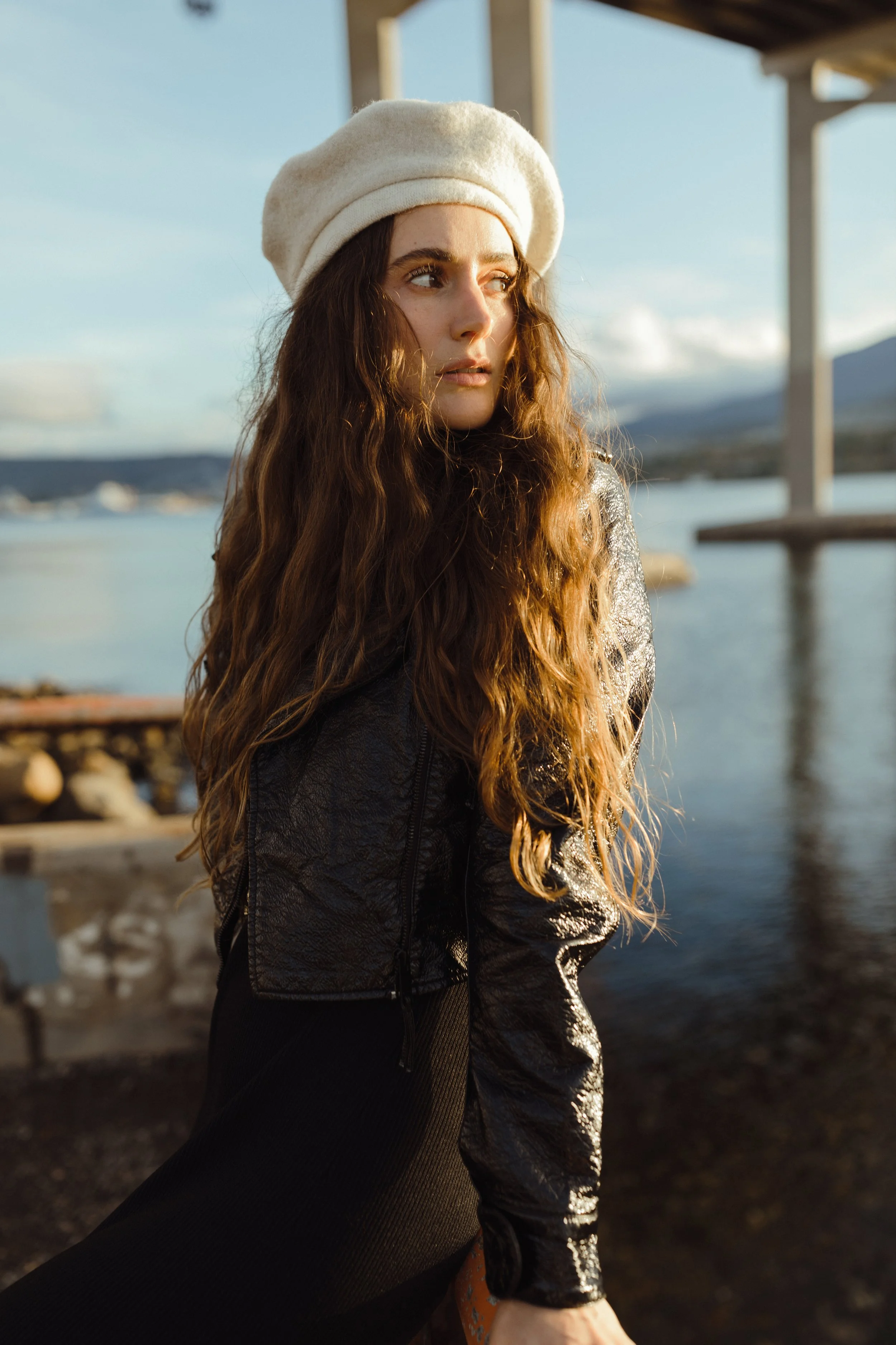 Fashion model poses beside river in white beret.