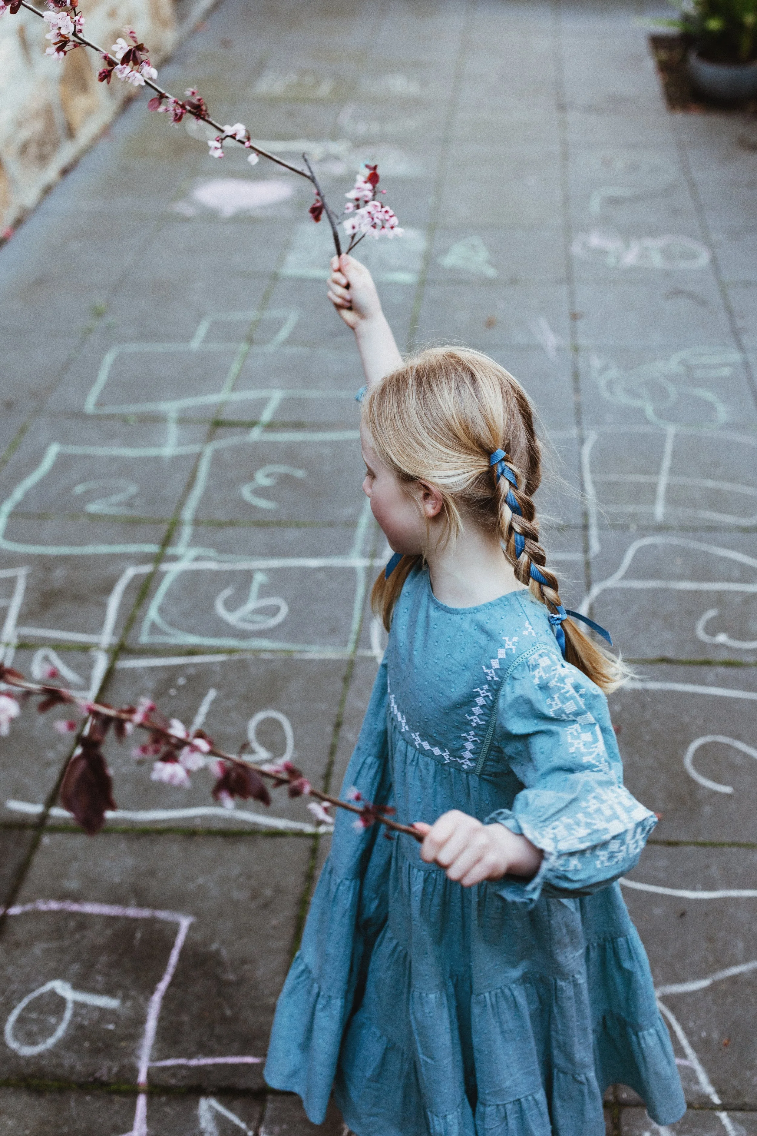 Young girl in blue dress plays in courtyard for children's fashion photo shoot.