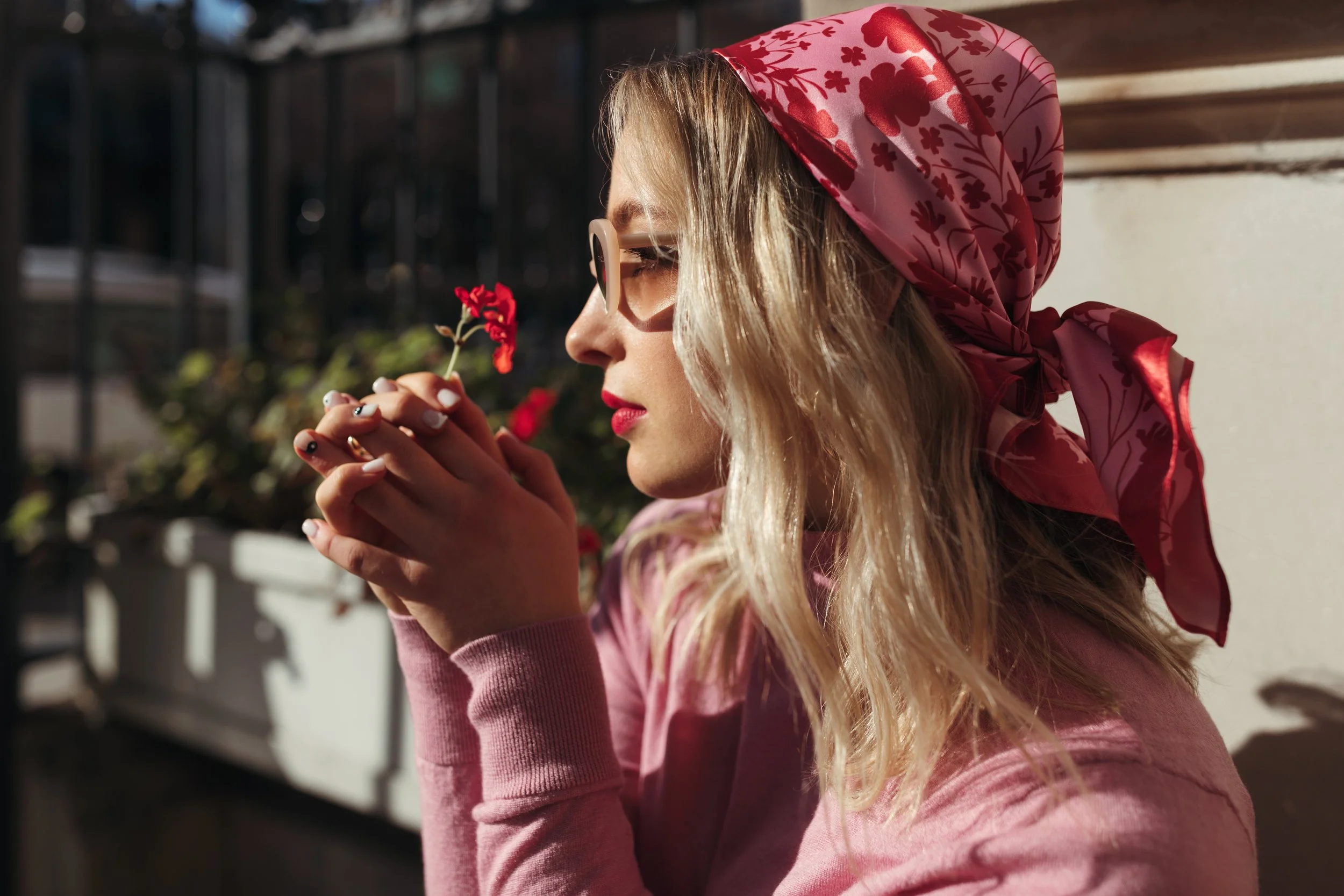 Model holds red flowers wearing pink and red head scarf.
