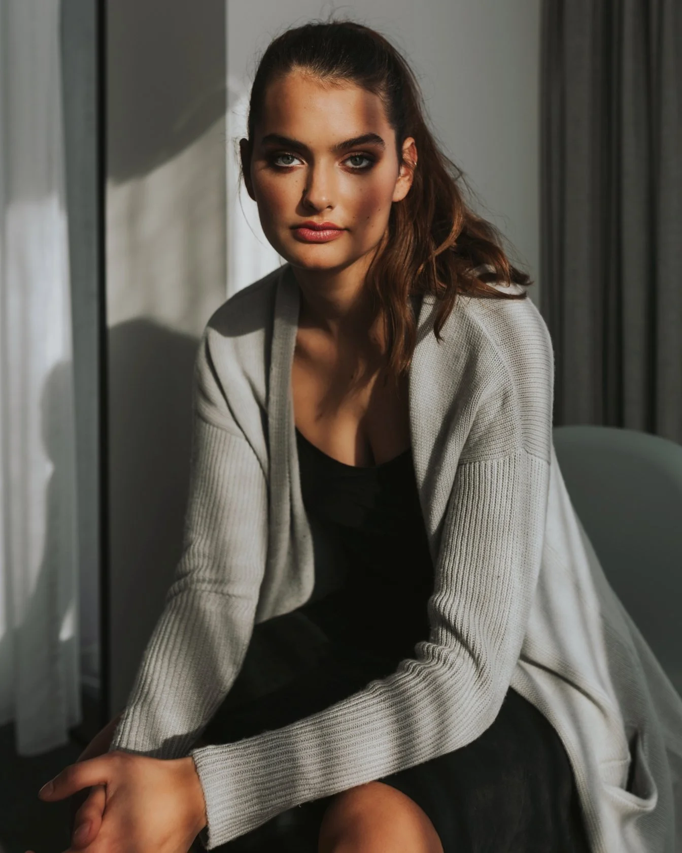 Fashion model sits beside window for commercial clothing shoot in Tasmania.