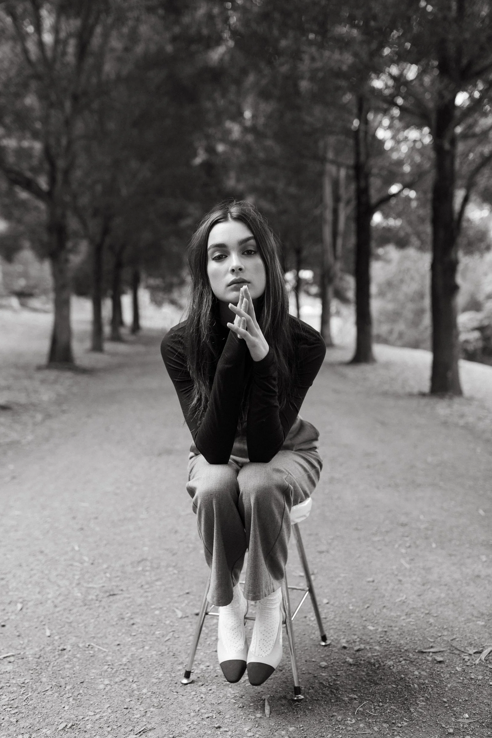 Model sits on stool on tree-lined footpath.