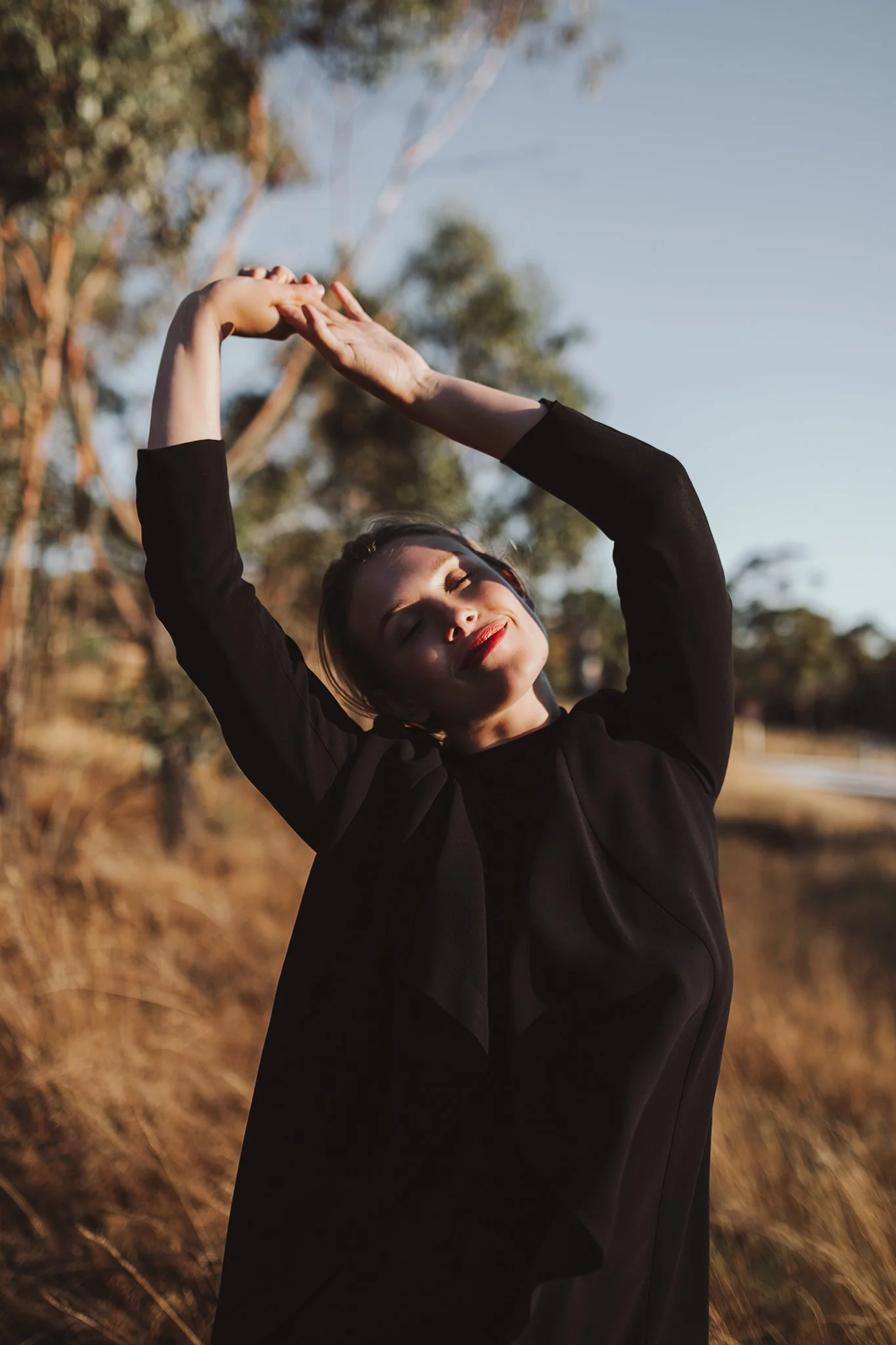 Model poses with arms in the air and smiling in a field.