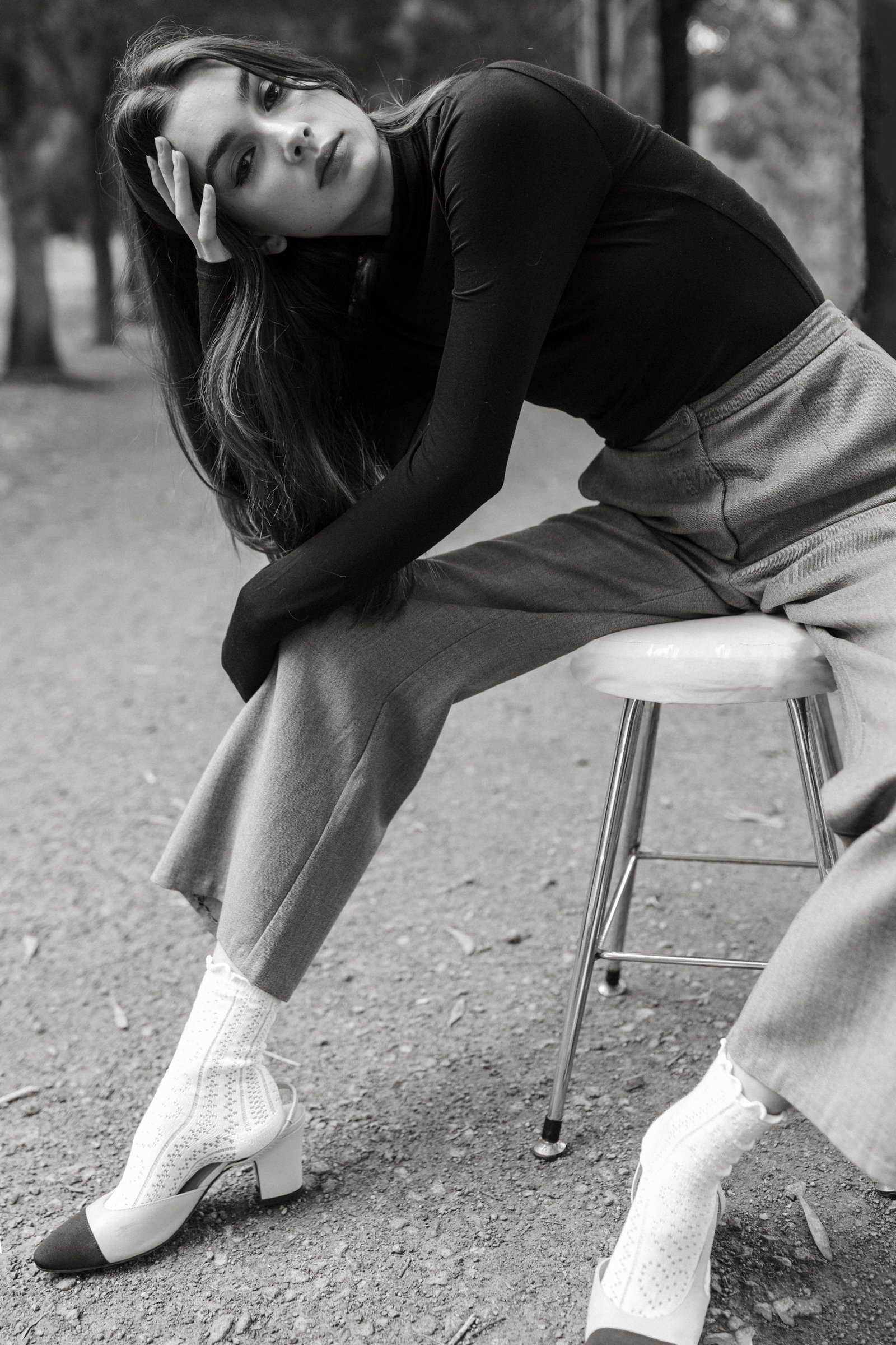 Woman poses on stool in park.
