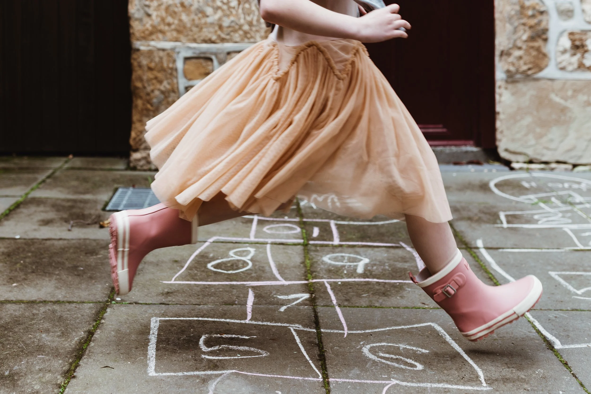 Girl runs across hopscotch in tulle dress.