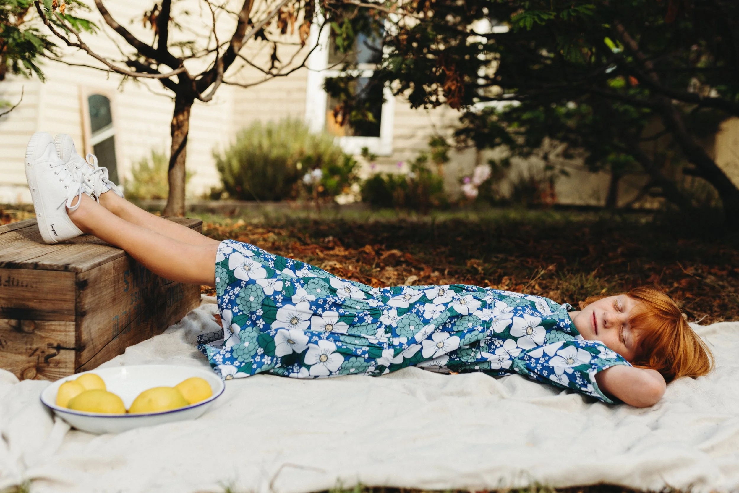 Girl lies on picnic rug with bowl of lemons for kids fashion shoot in Tasmania.