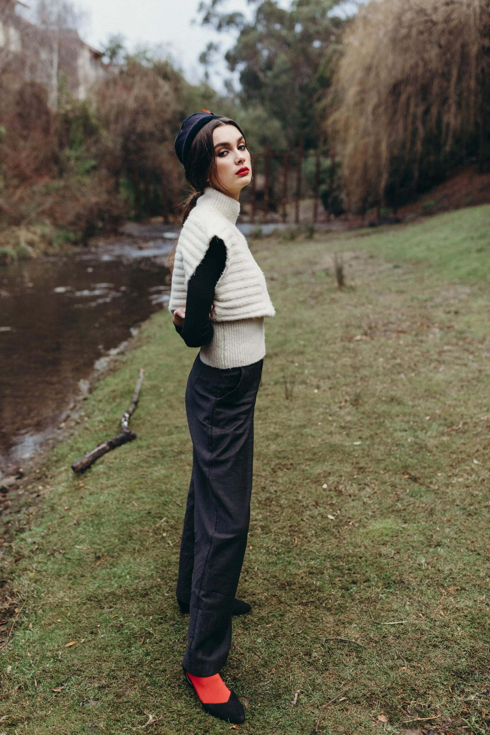 Model stands beside water in Tasmania in vintage outfit.