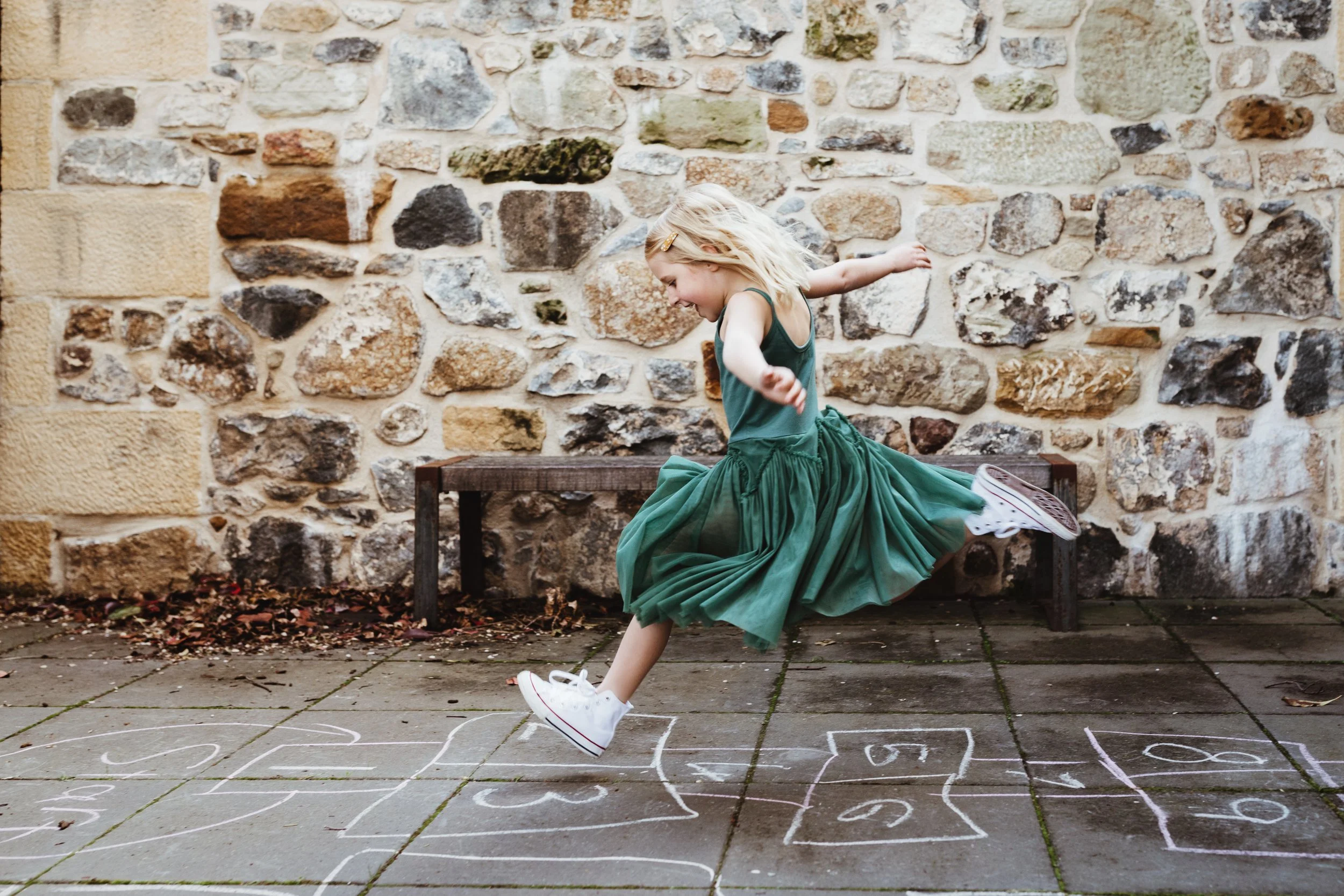 Blonde girl jumps over hopscotch game in kids clothing photo shoot.