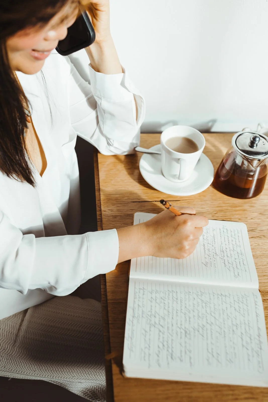 Woman writes in notebook as she speaks on the phone in Hobart cafe.