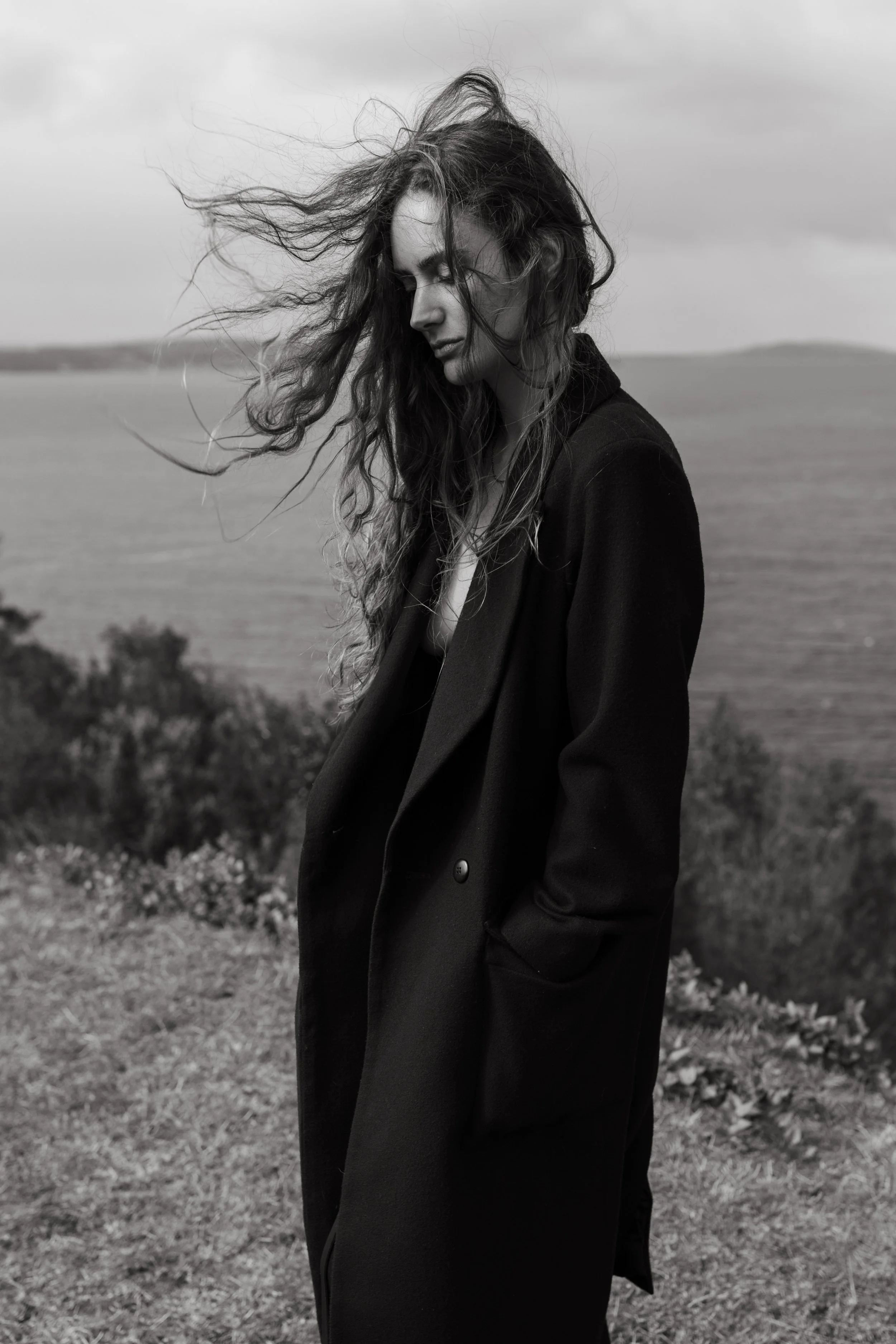 Fashion model stands on headland with wind blowing in Hobart, Tasmania.