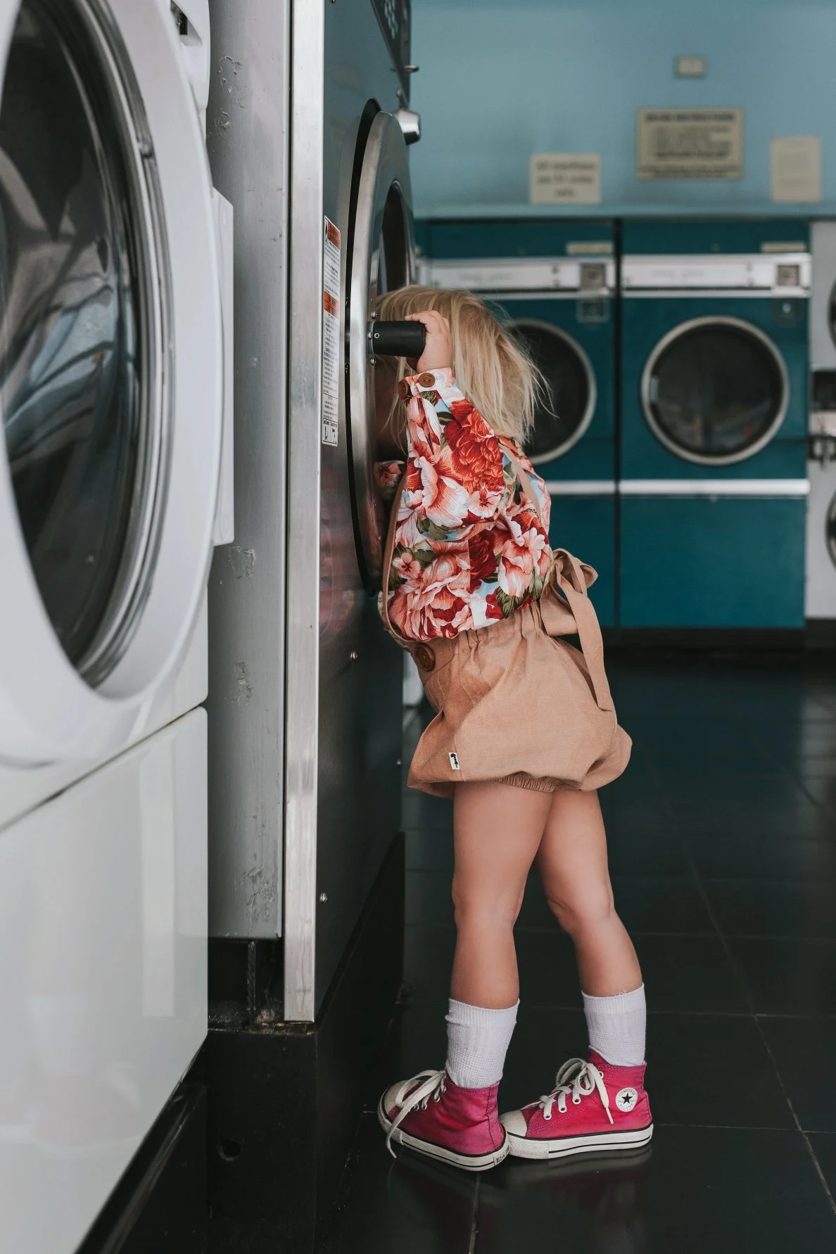 Young girl looks in washing machine at laundromat for styled photo shoot.