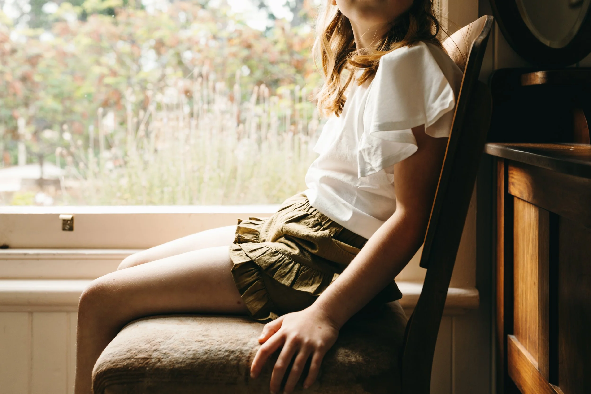 Young girls sits beside window for kids clothing label photo shoot.