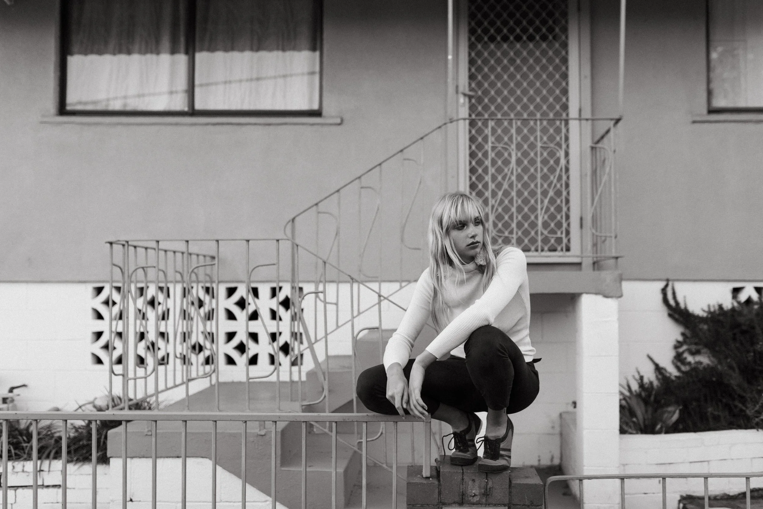 Woman crouches on fence during photo shoot.