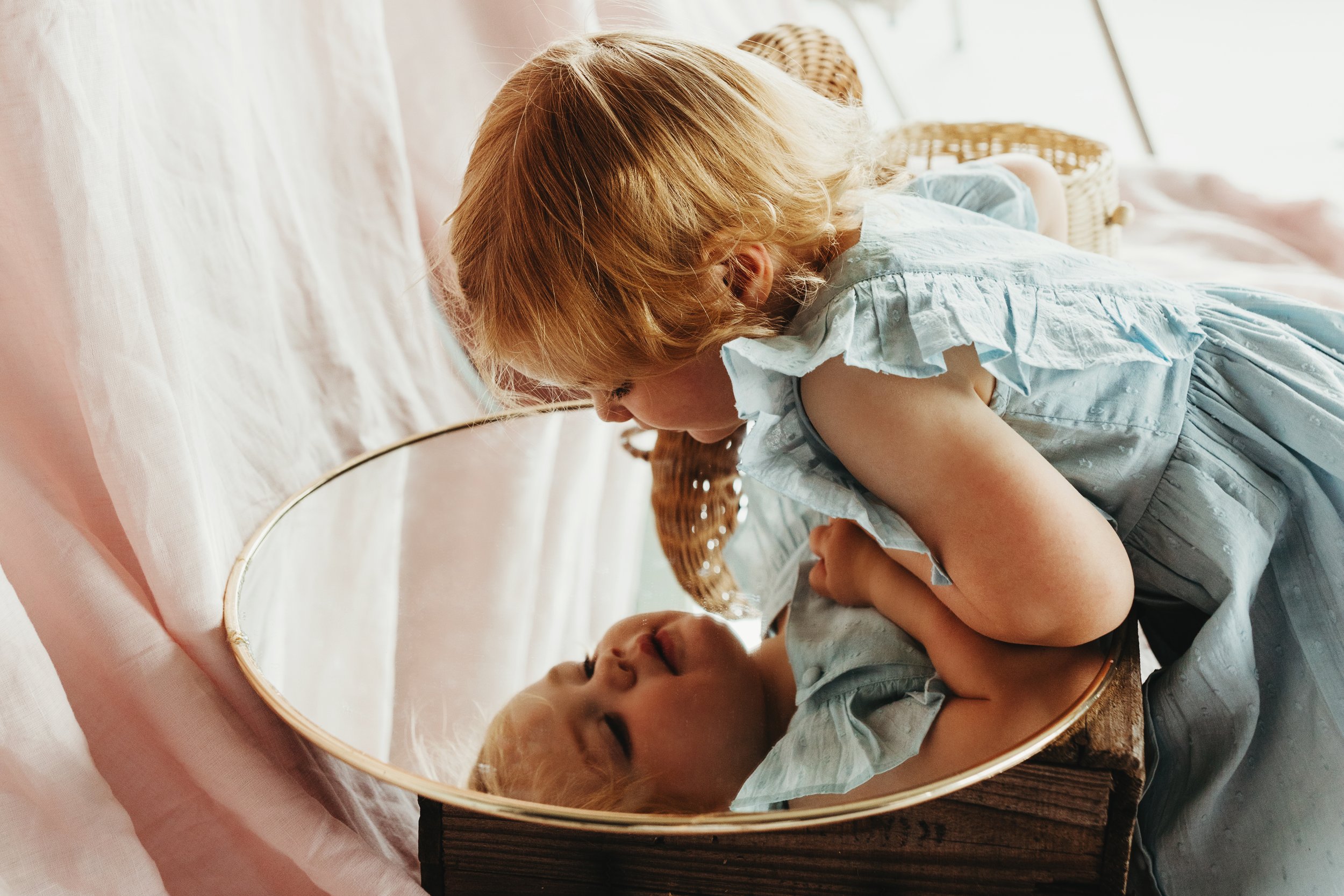 Toddler looks into mirror wearing fashionable dress.