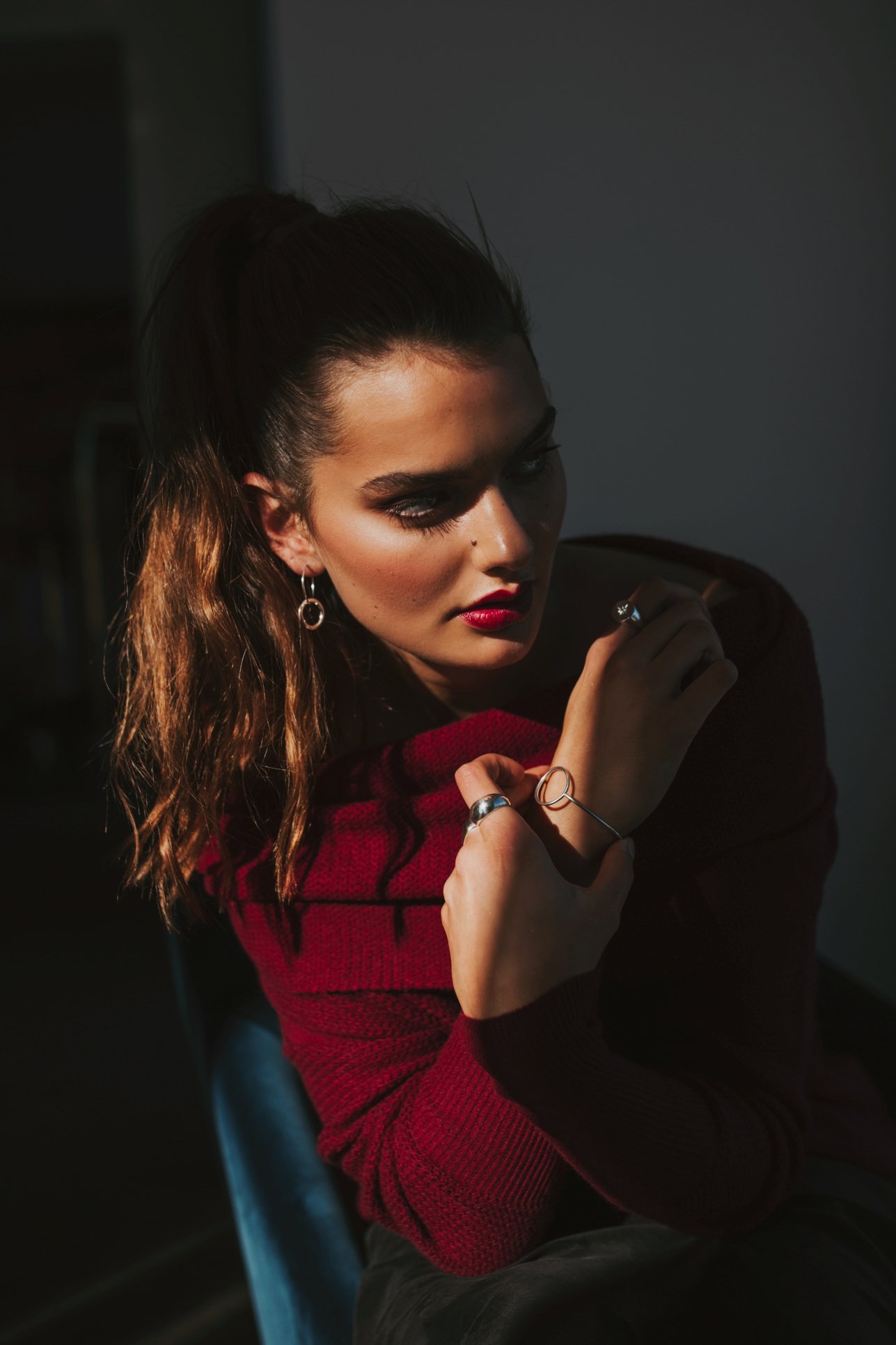 Model sits in blue chair and poses wearing wine red cashmere.