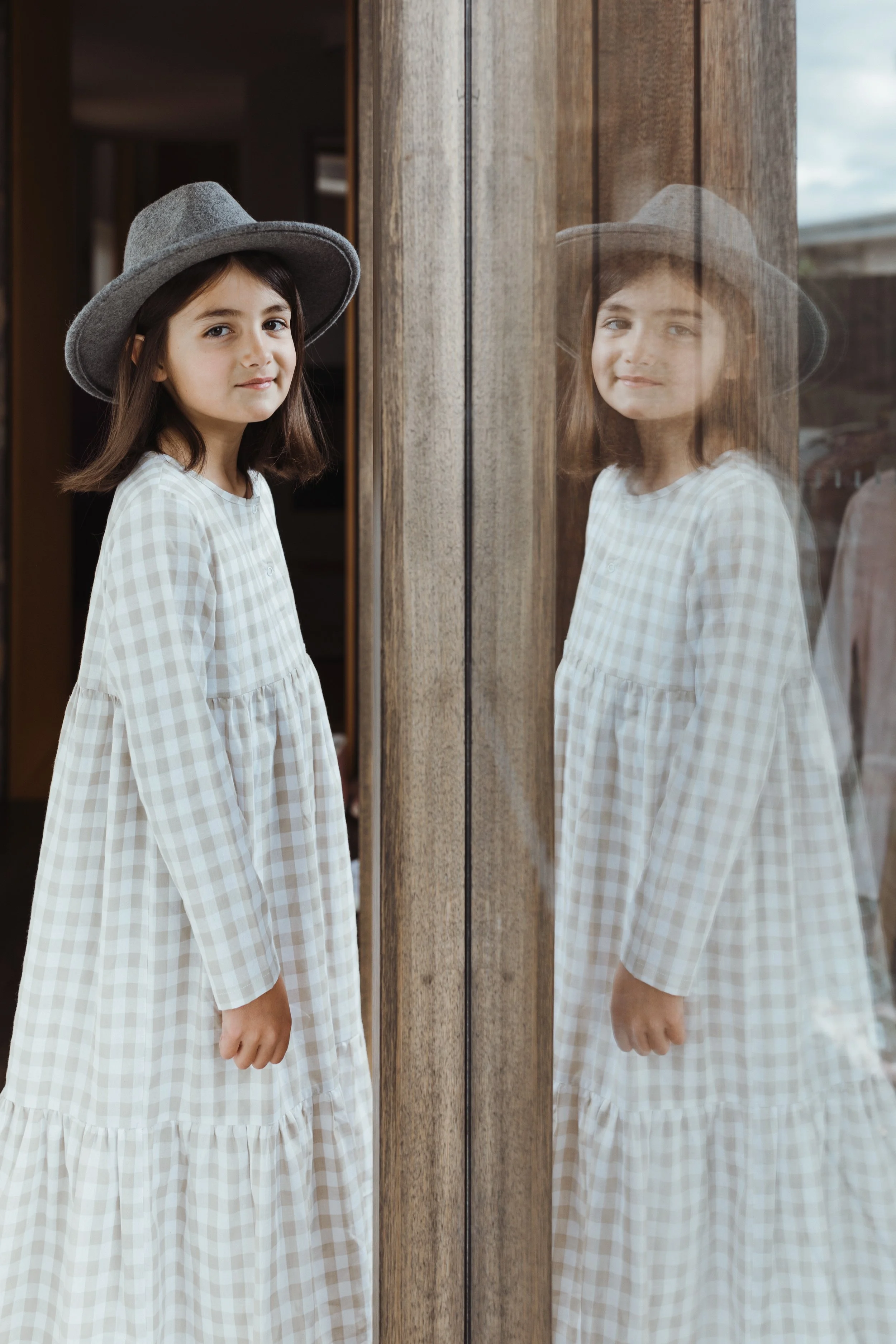Young girl stands in gingham dress and hat for kids fashion photography shoot in Hobart.