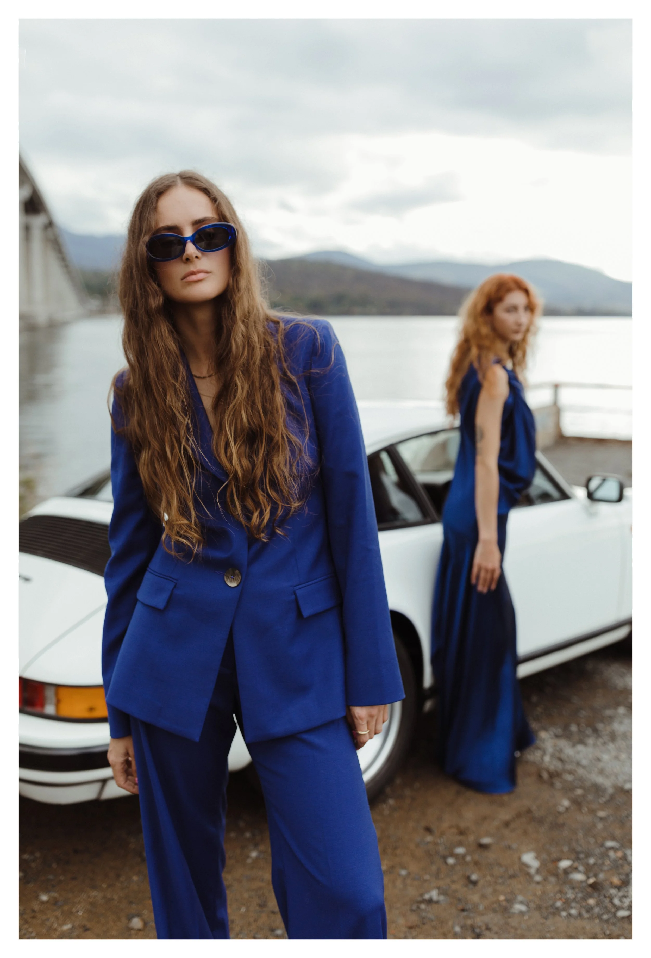 Model wears blue suit in front of white vintage porsche for fashion photo shoot.