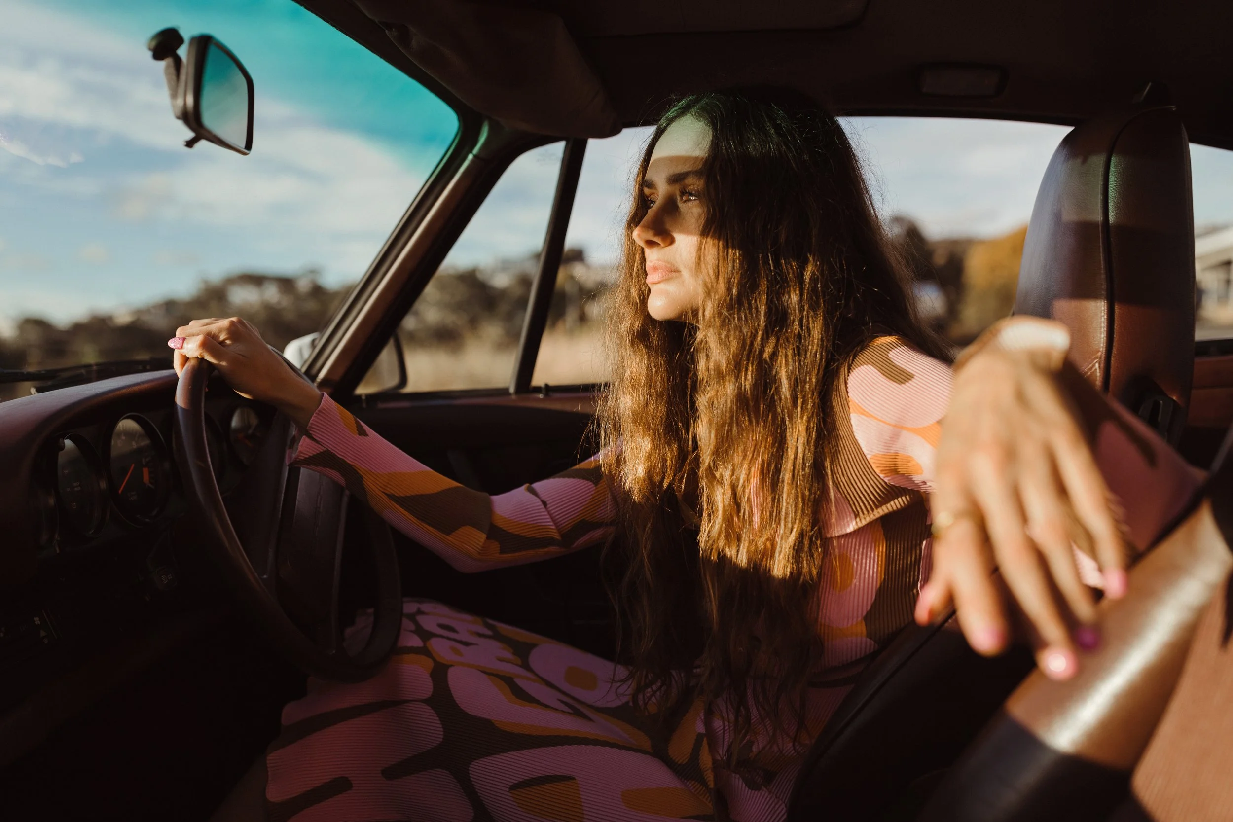 Styled photograph of fashionable woman in old car looking in mirror.