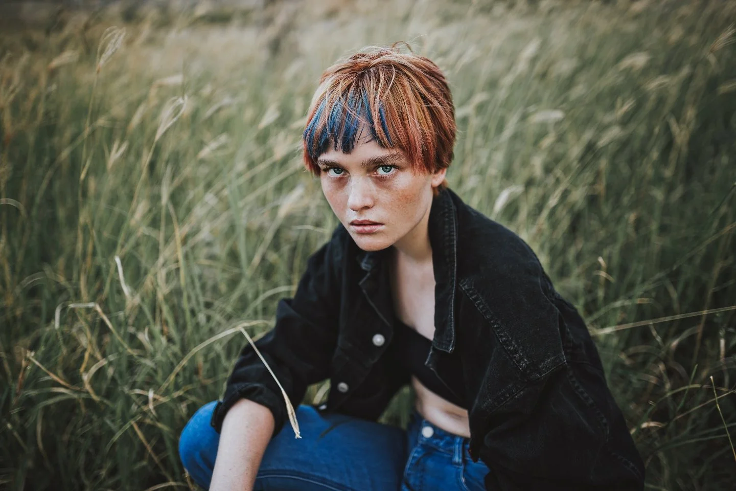 Model crouches in grass during fashion photography.
