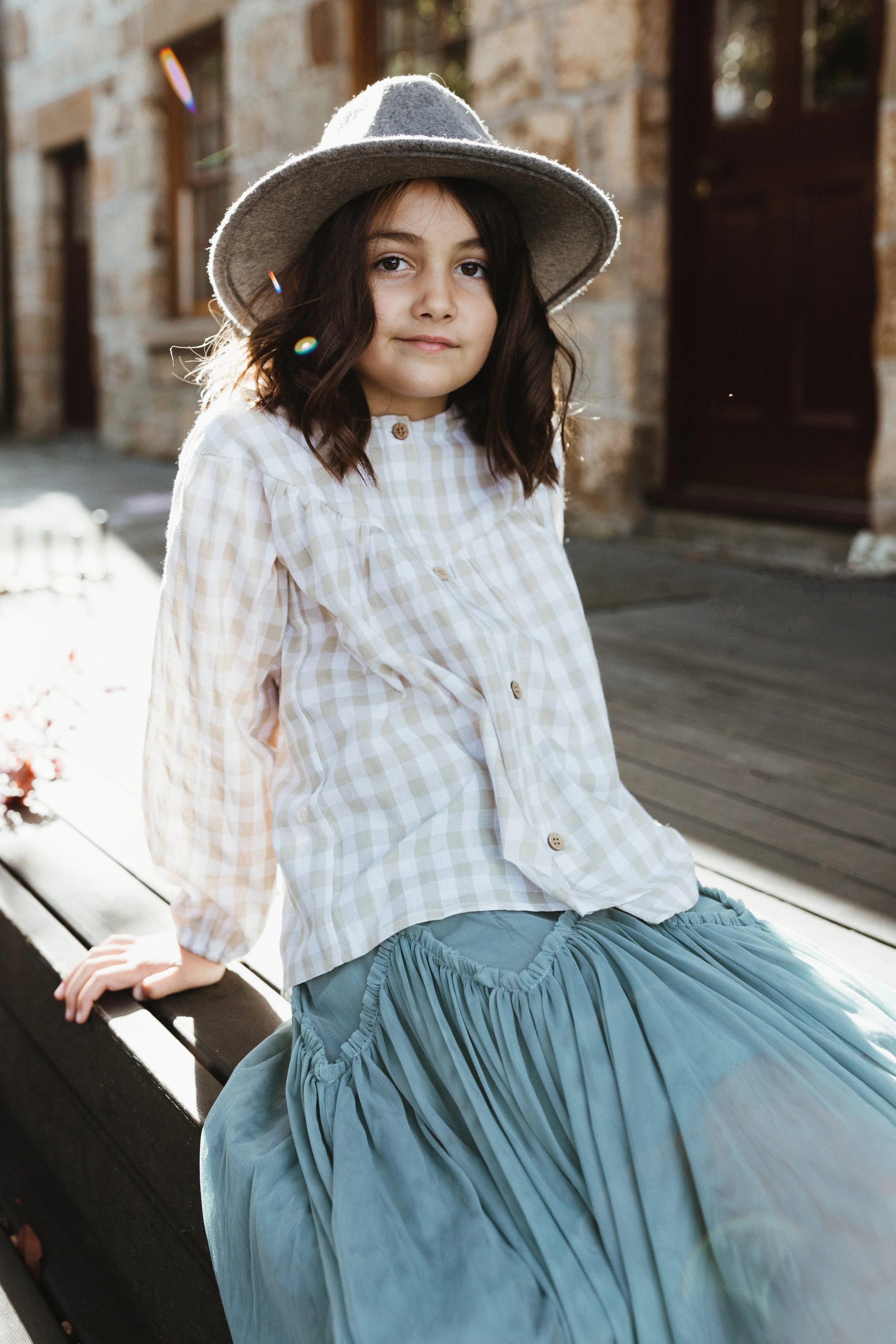 Young girl sits in courtyard with sun behind her wearing grey hat in Hobart.