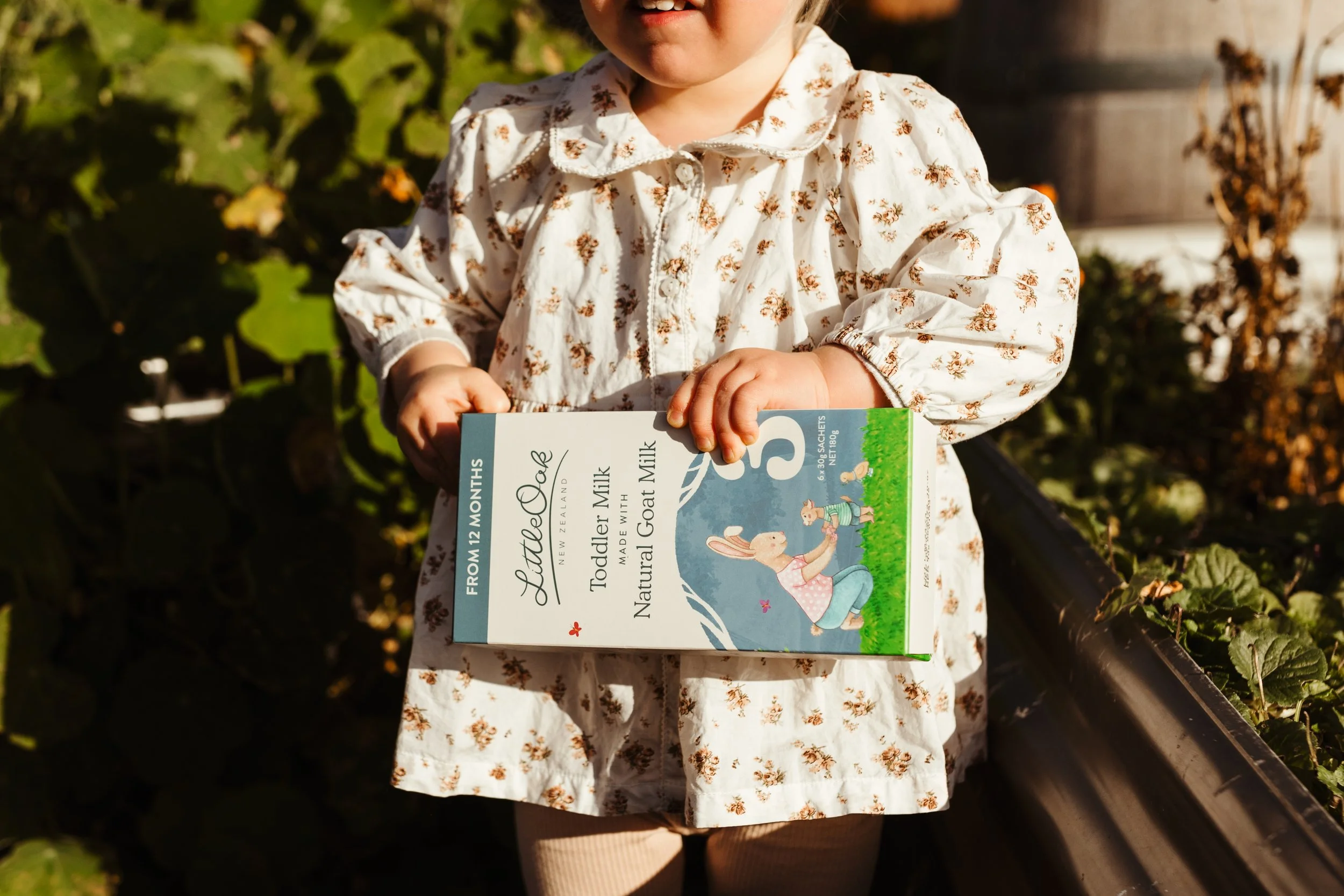 Child holds baby product in garden at event brunch.