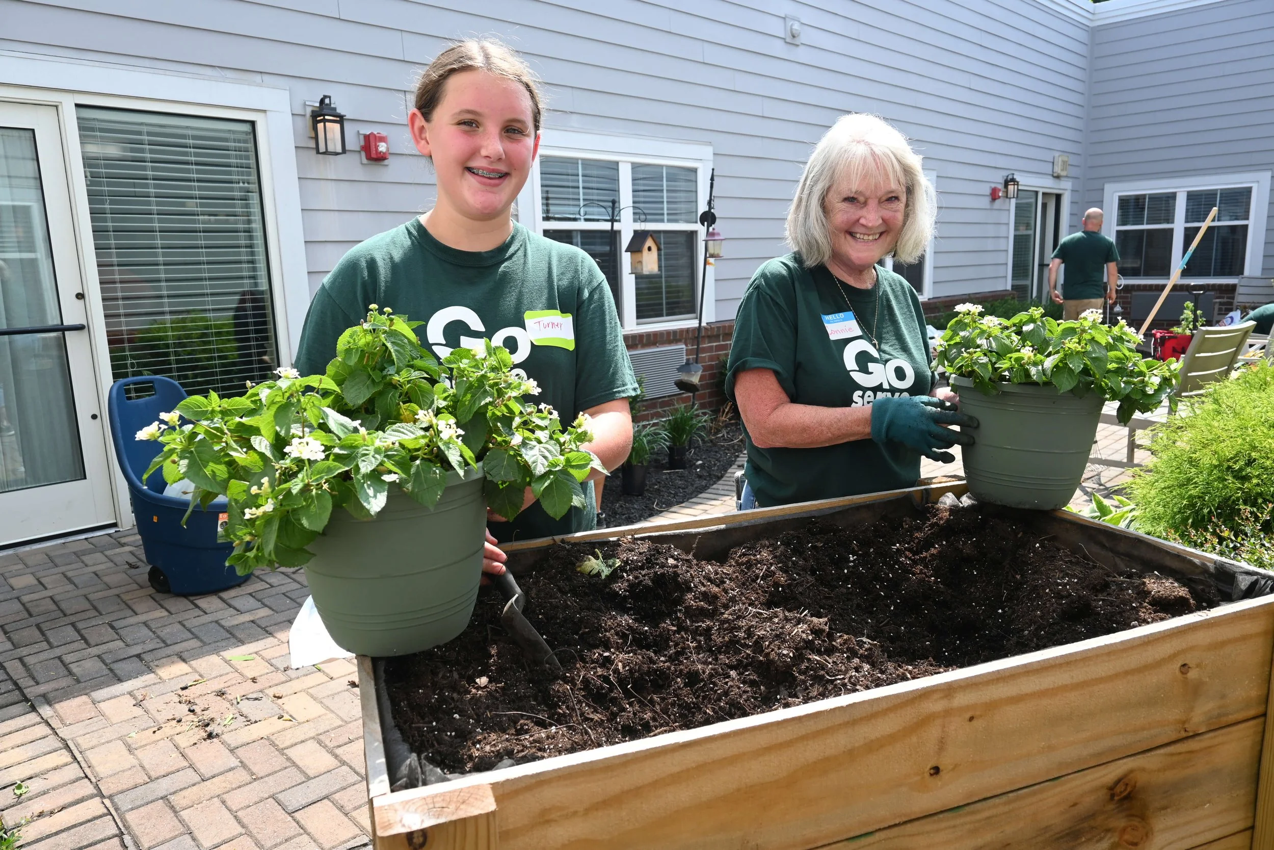 tween girl and retired woman planting in raised garden bed